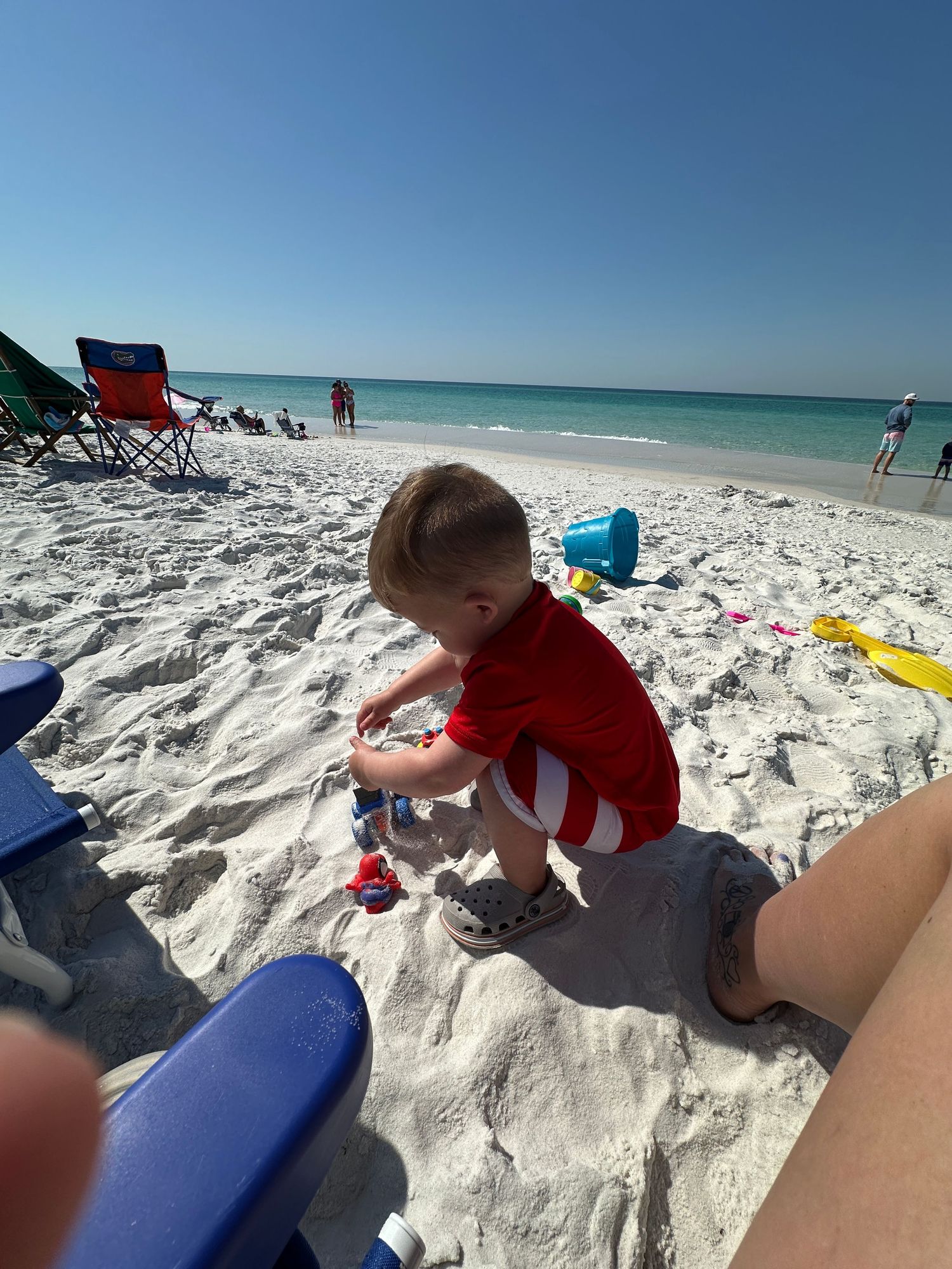 Child playing in pristine white sand on a beautiful beach with turquoise waters and clear blue skies.