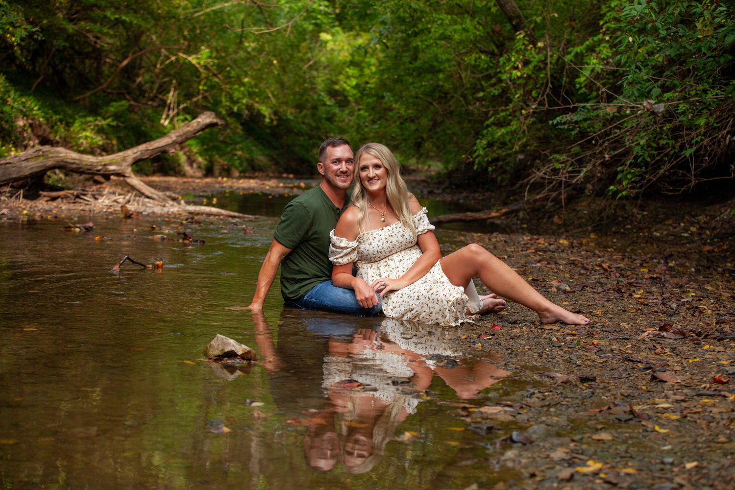 Couple in white outfits sharing intimate moments by a creek during a romantic outdoor photo session.