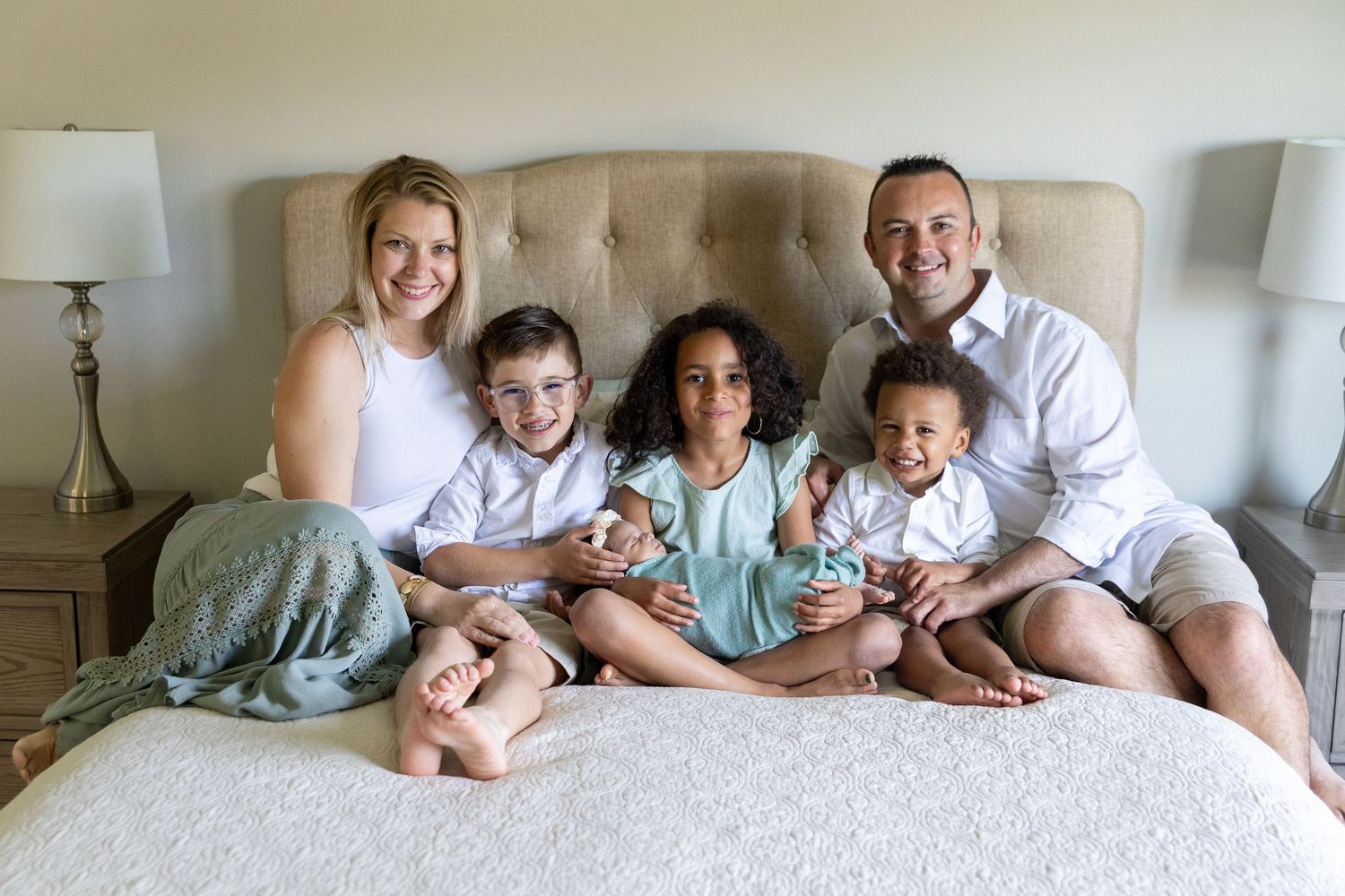 Casual family portrait on bed with everyone wearing white and light colored clothing.