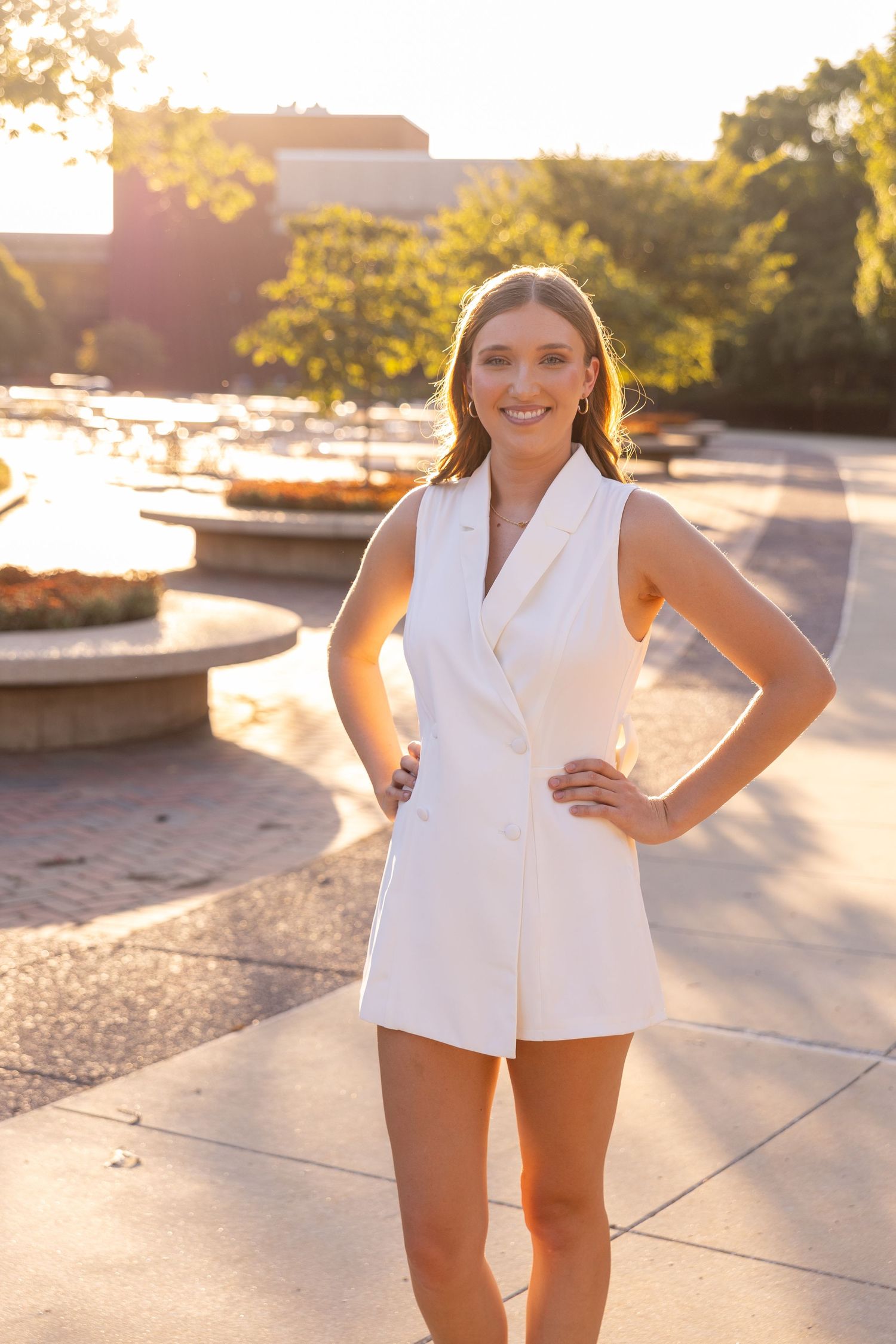Woman in white sleeveless romper posing outdoors during golden hour.