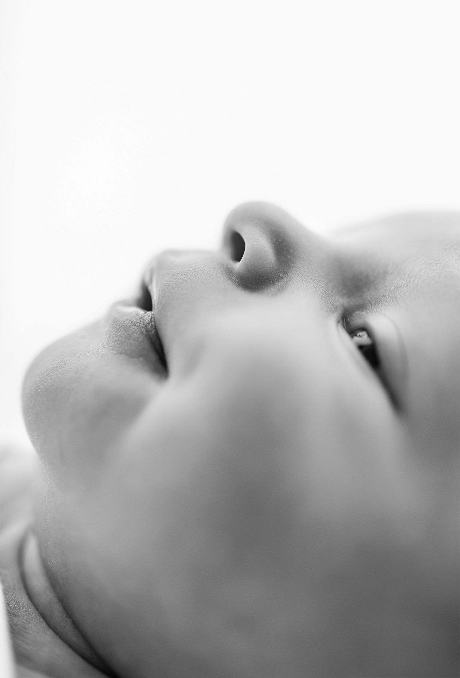 Close-up black and white portrait of a newborn baby face looking upward, showcasing delicate features.