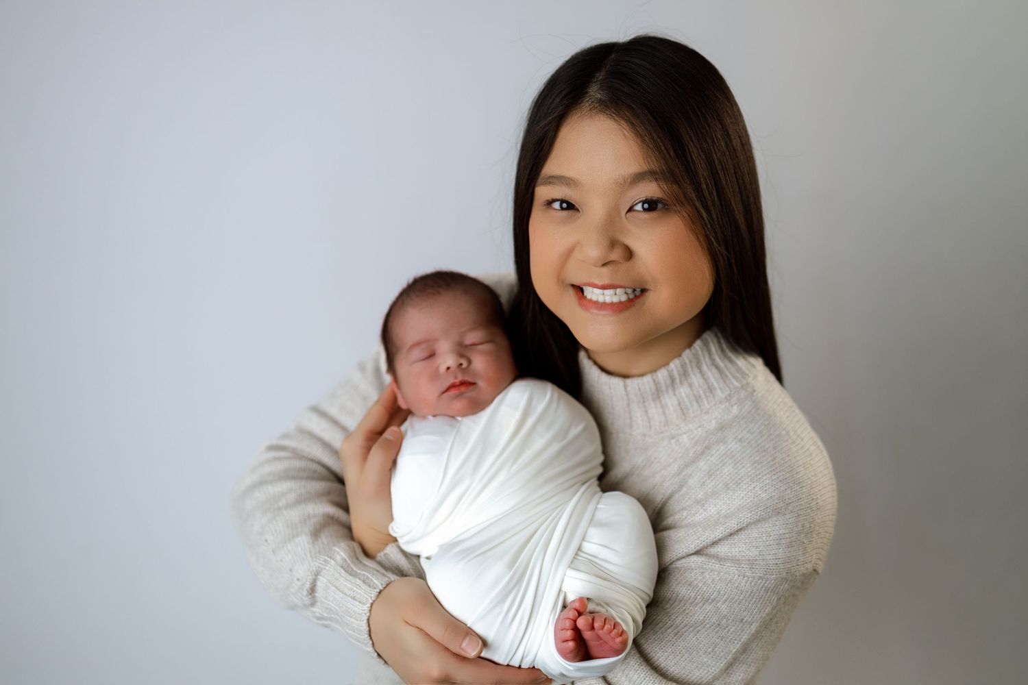 A newborn baby wearing white clothing rests in someone's arms while being photographed from multiple angles.