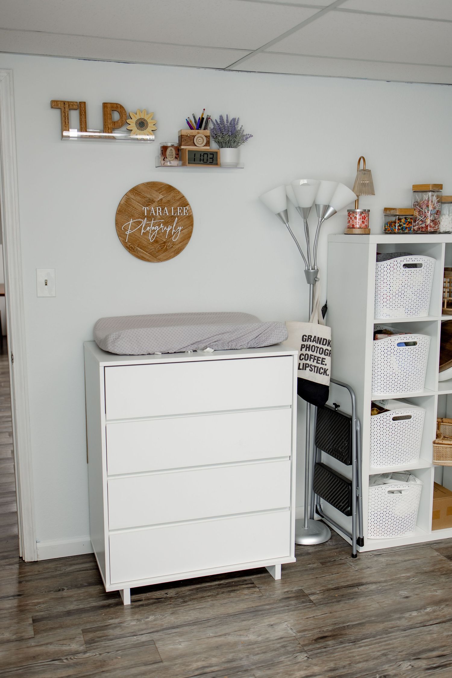 White storage furniture with drawers arranged against a wall with decorative items and wood flooring.