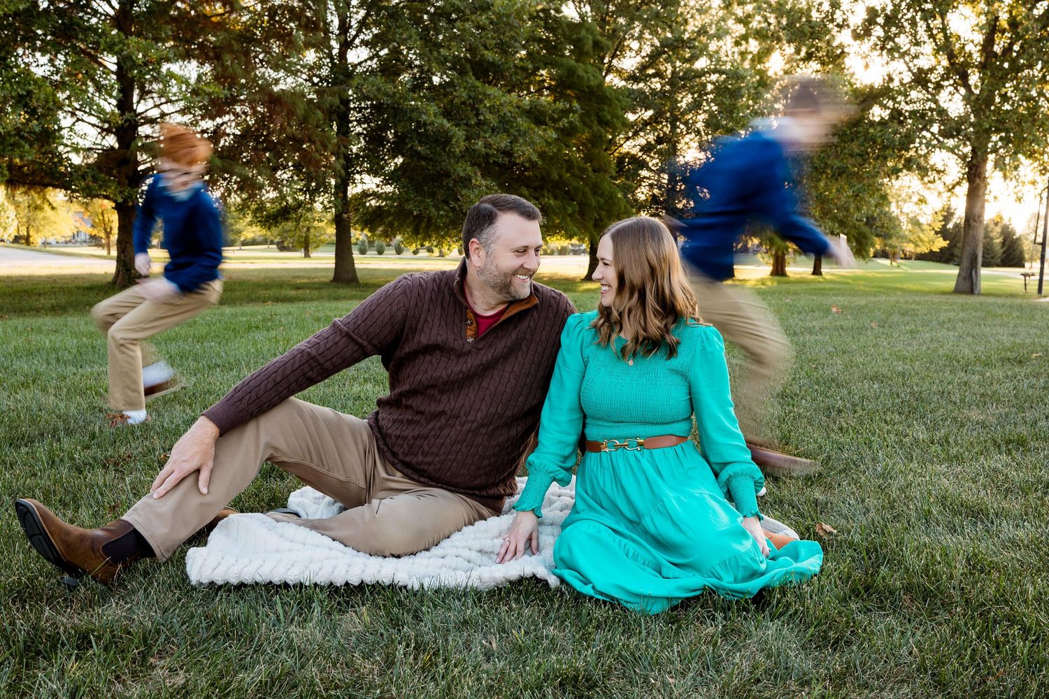 A couple relaxes together on green grass during a warm sunset in a park setting.