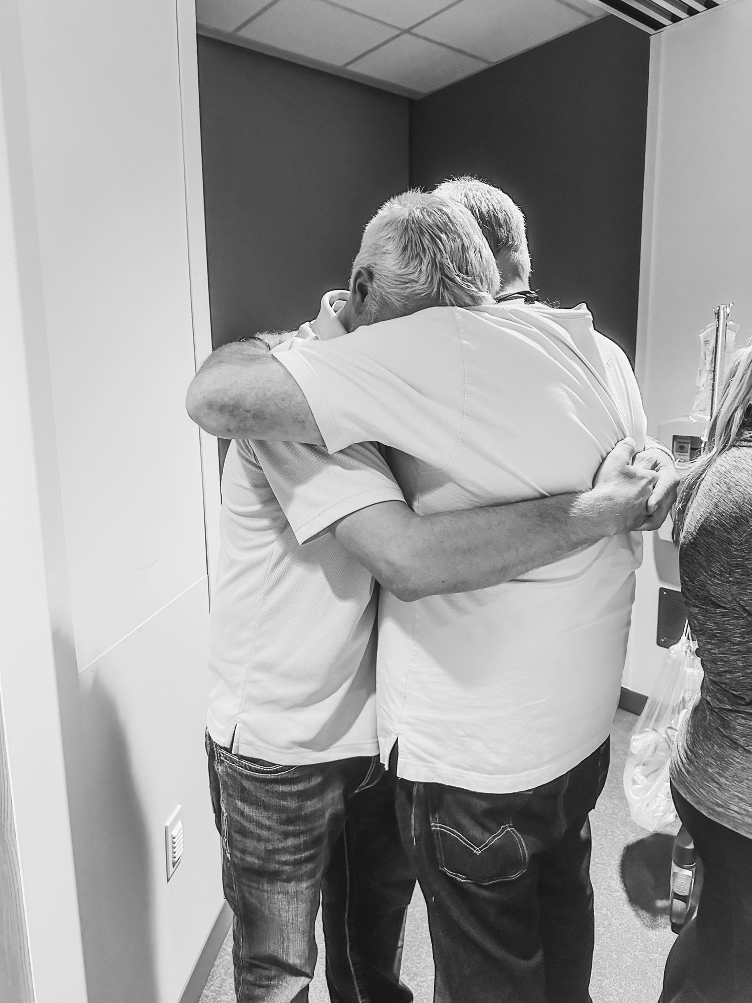 Two people share emotional embrace in hospital corridor wearing white shirts.