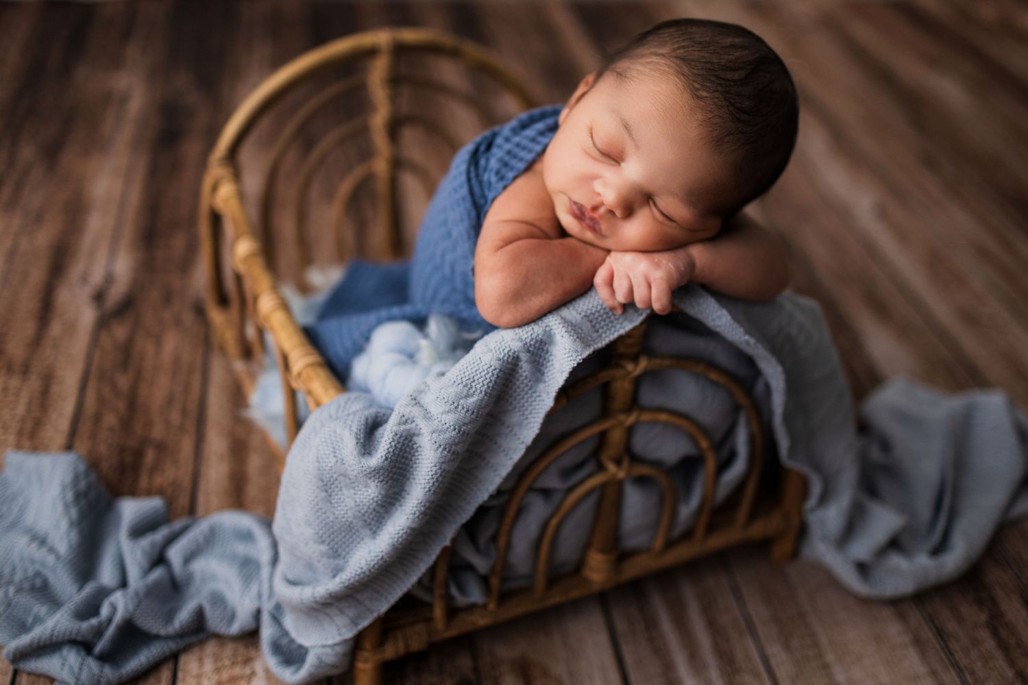 A baby wearing gray pajamas lies sleeping on a wooden spindle bed with a brown ornamental headboard.