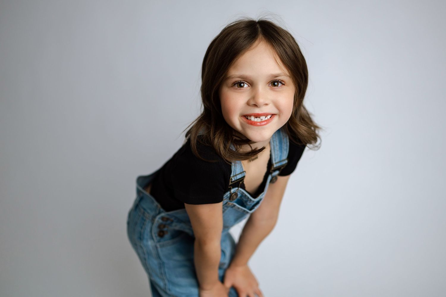 Child in denim dress poses playfully in multiple candid studio portraits against light background.