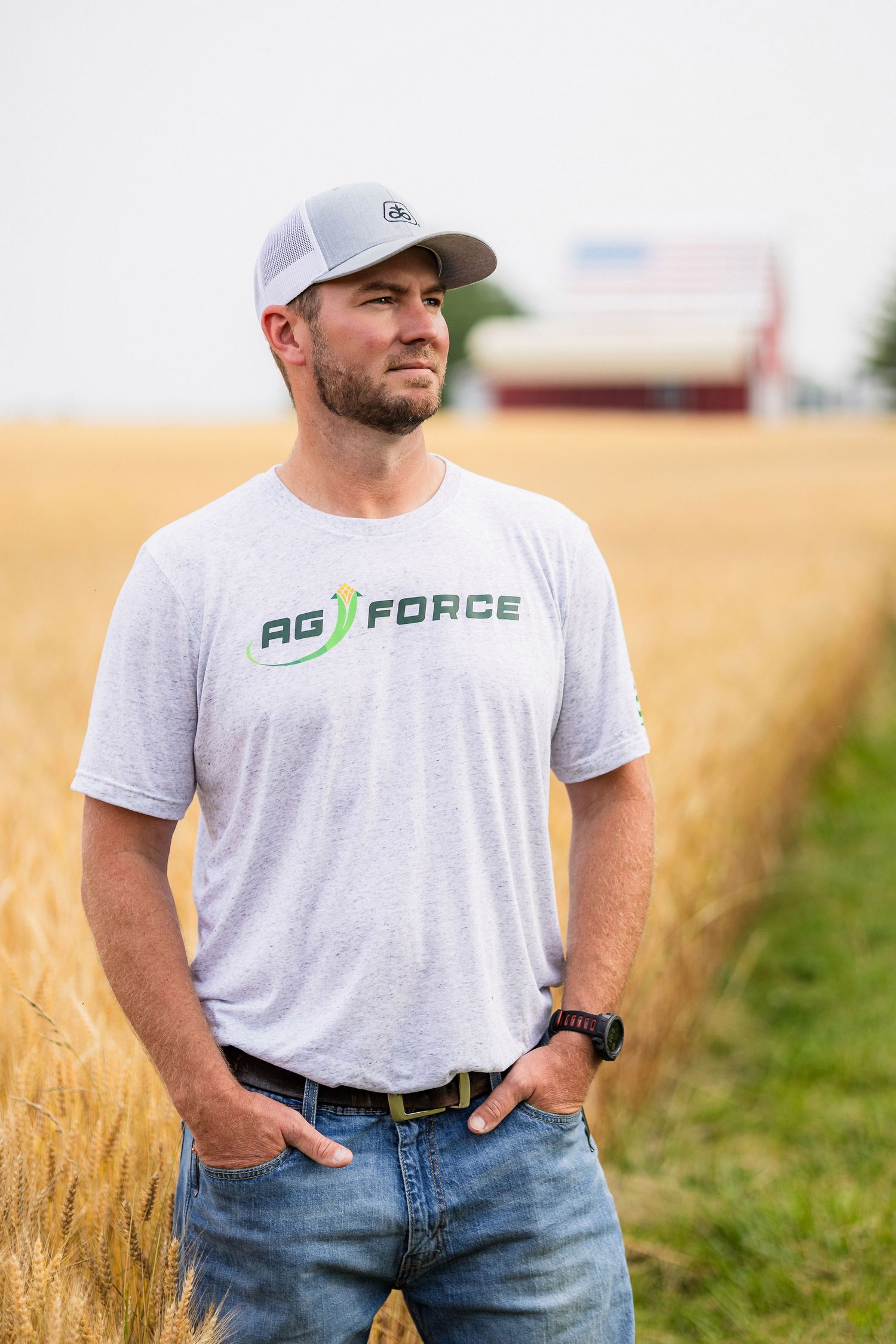 Farmer wearing white t-shirt and jeans standing in wheat field at harvest time.