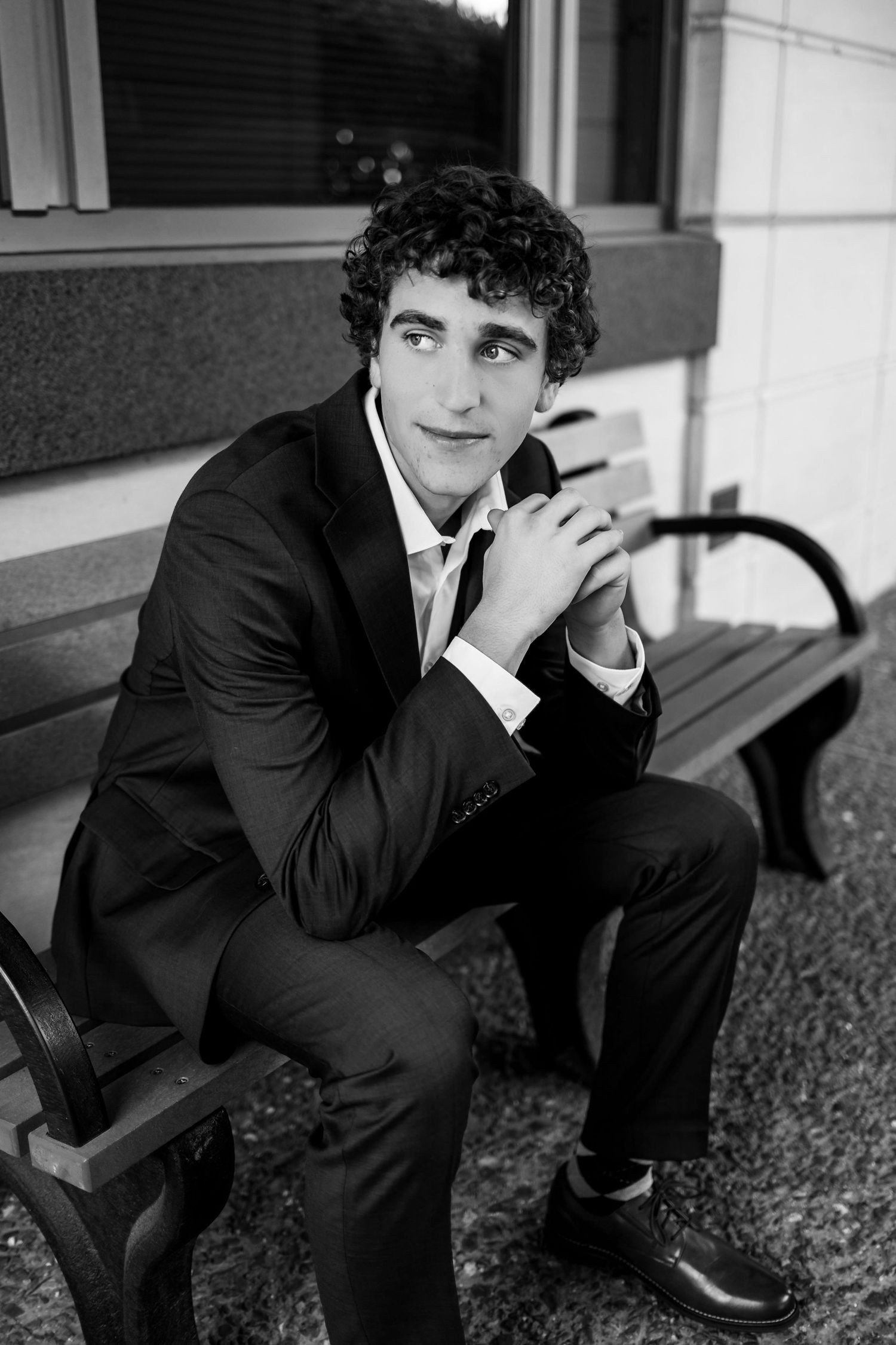 Young man in dark suit sits thoughtfully on outdoor steps in black and white portrait series.