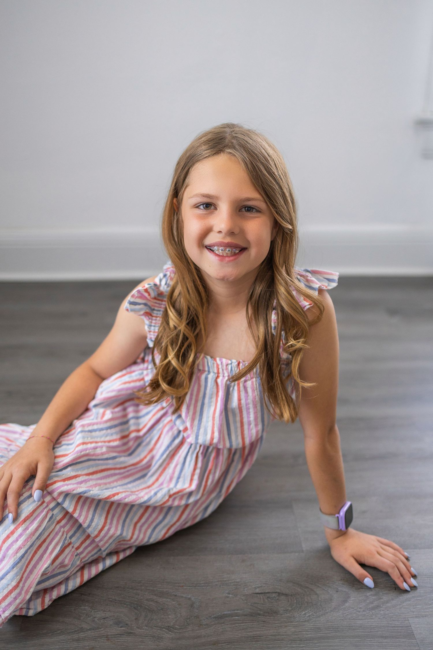 Young person lying on grey floor wearing striped pink and white summer dress with ruffled sleeves.