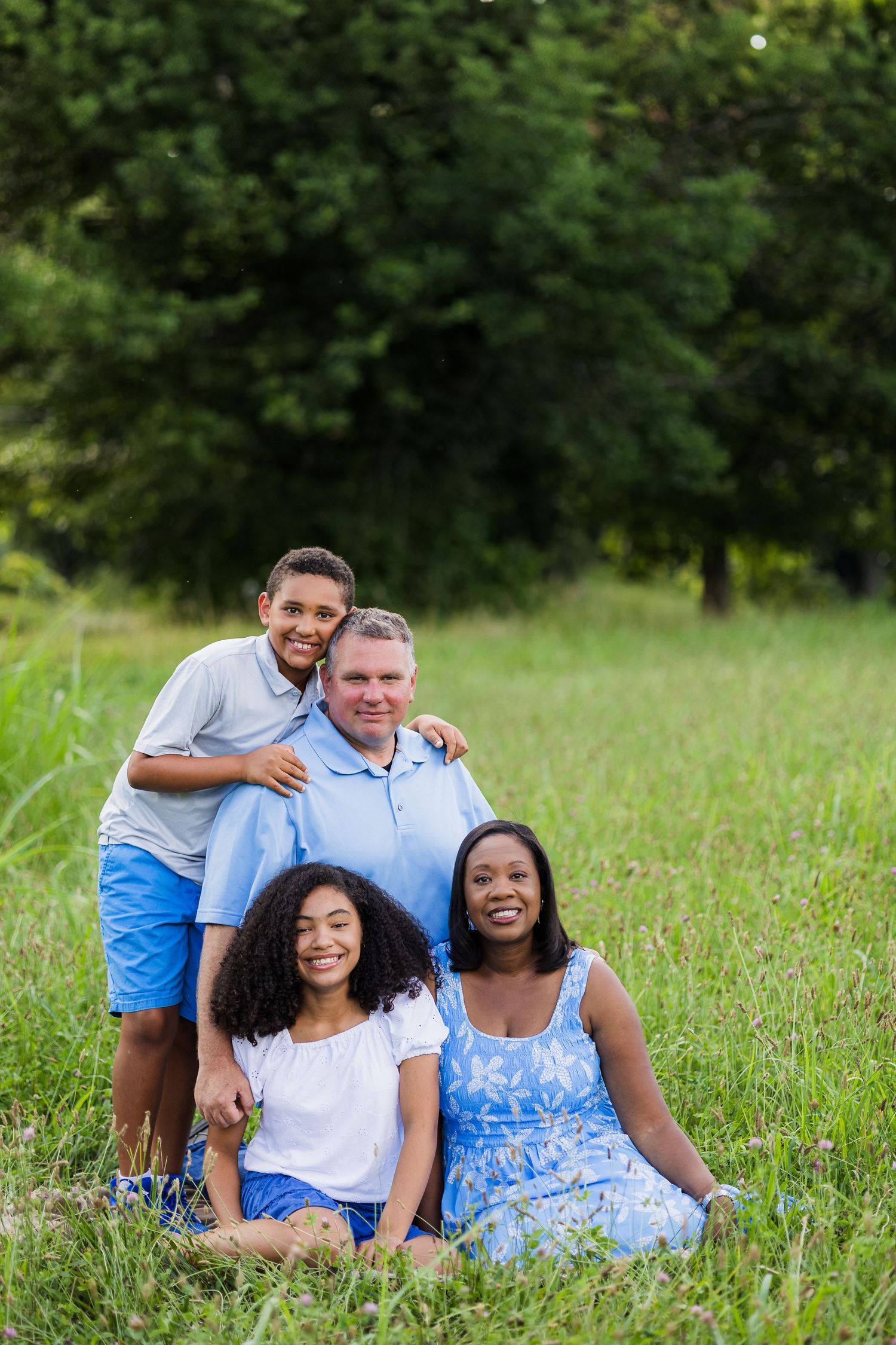 Happy family sitting together in a grassy field on a sunny summer day.
