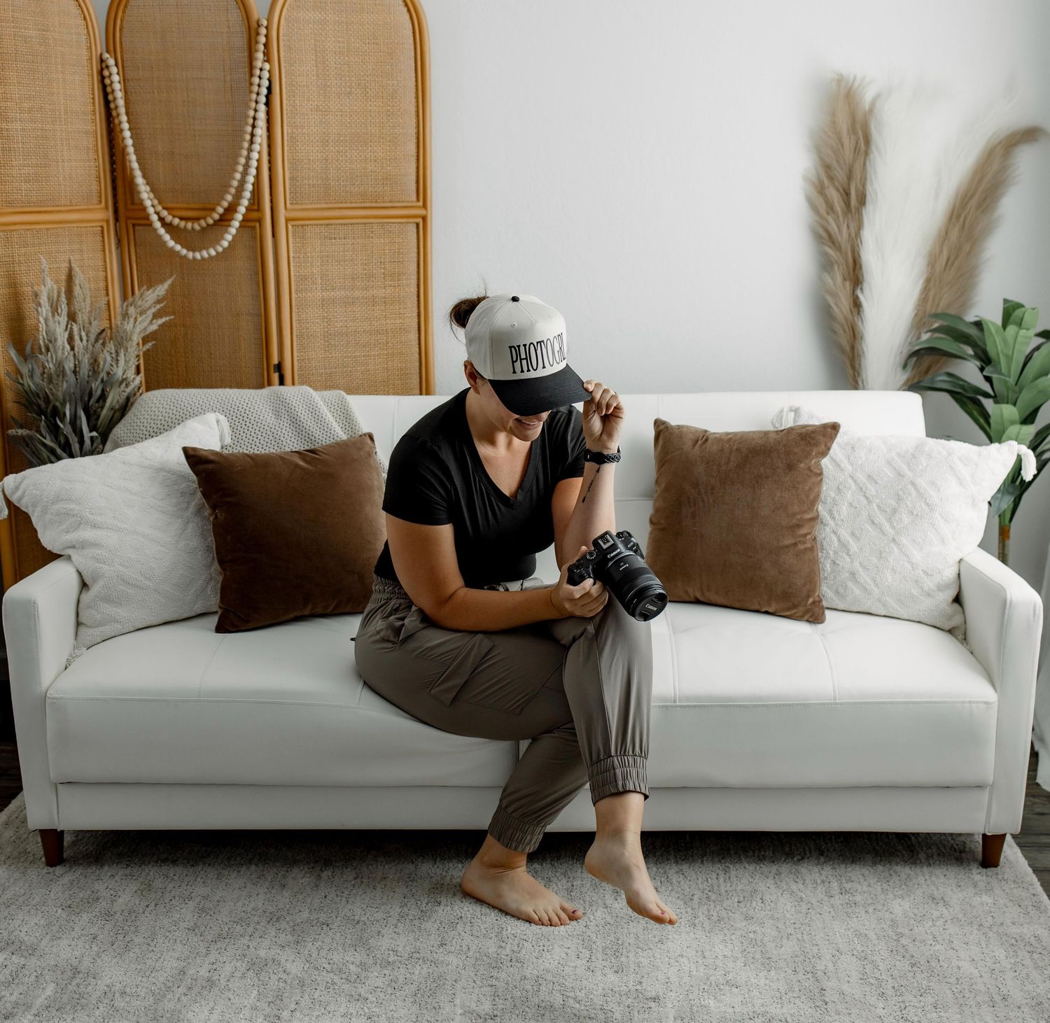 Person sitting on a white couch with brown throw pillows in a modern minimalist living room setting.