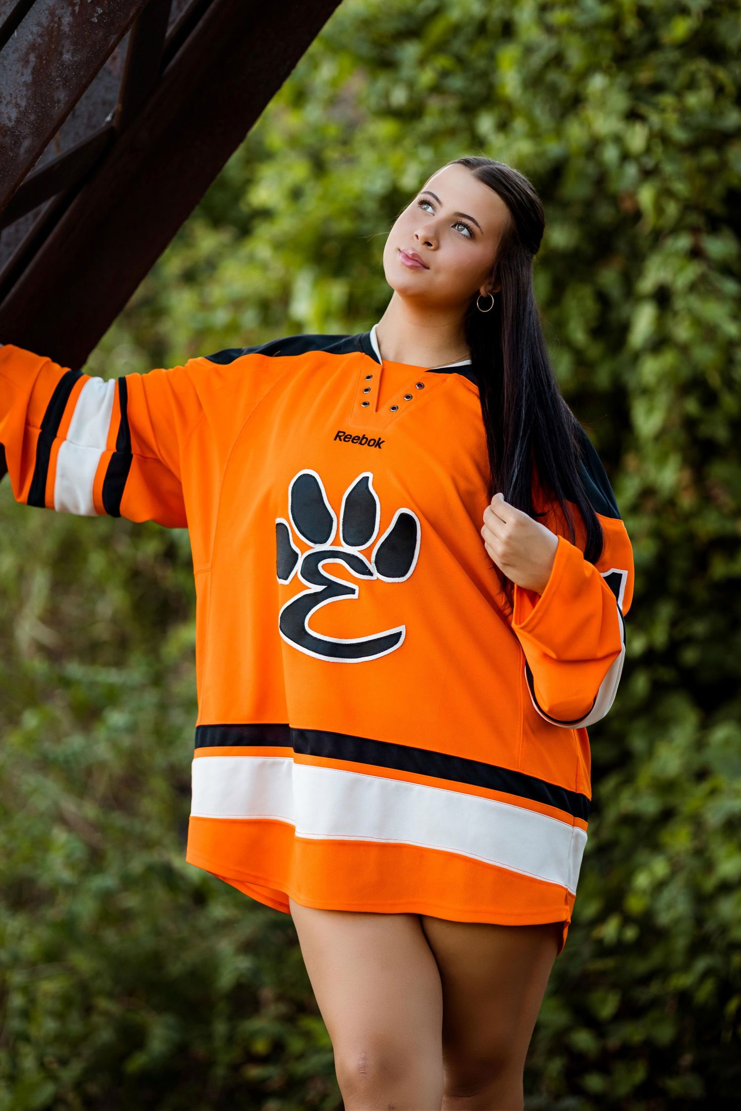 Orange hockey jersey with black paw print logo shown in creative outdoor fashion poses against green foliage background.