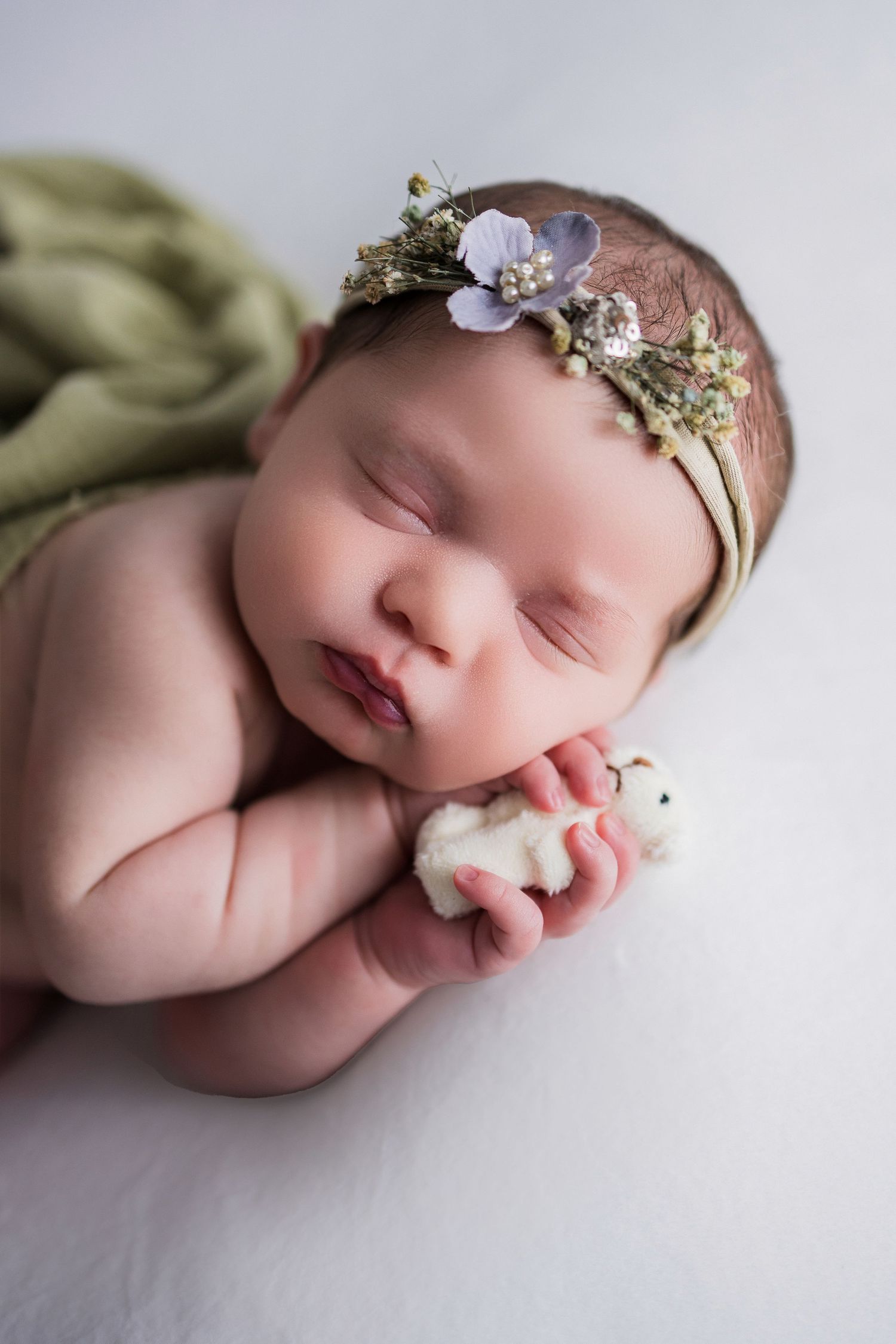 A sleeping newborn baby lies peacefully wearing a delicate floral headband in a professional portrait session.
