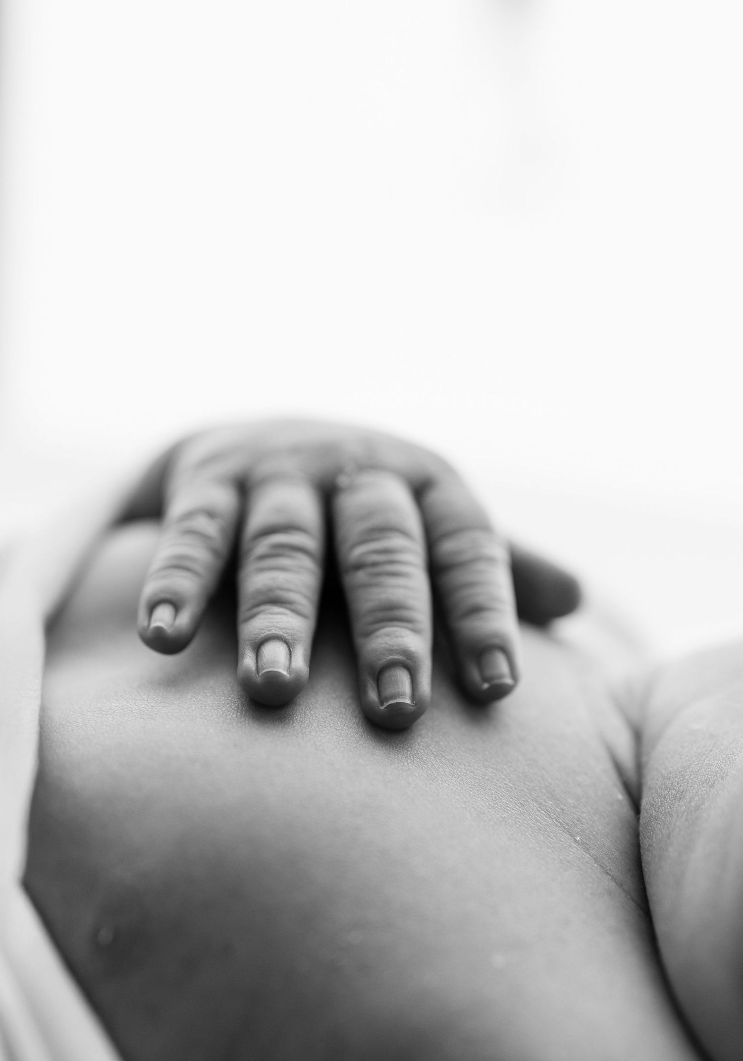 Close-up black and white photo of a hand resting gently on a pregnant belly, showcasing maternity beauty.