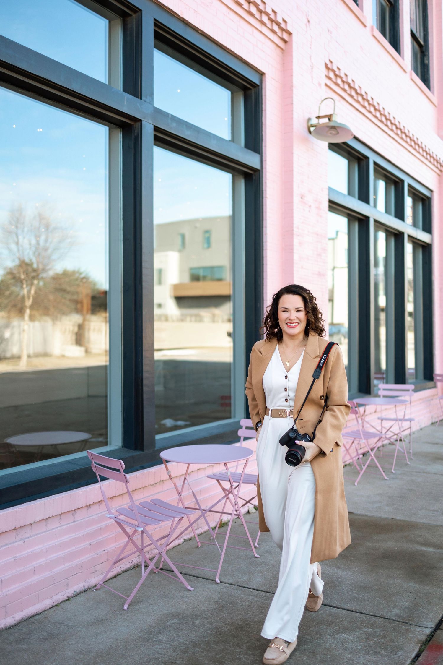 A stylish lifestyle photoshoot outside a modern building with pink chairs and large windows.
