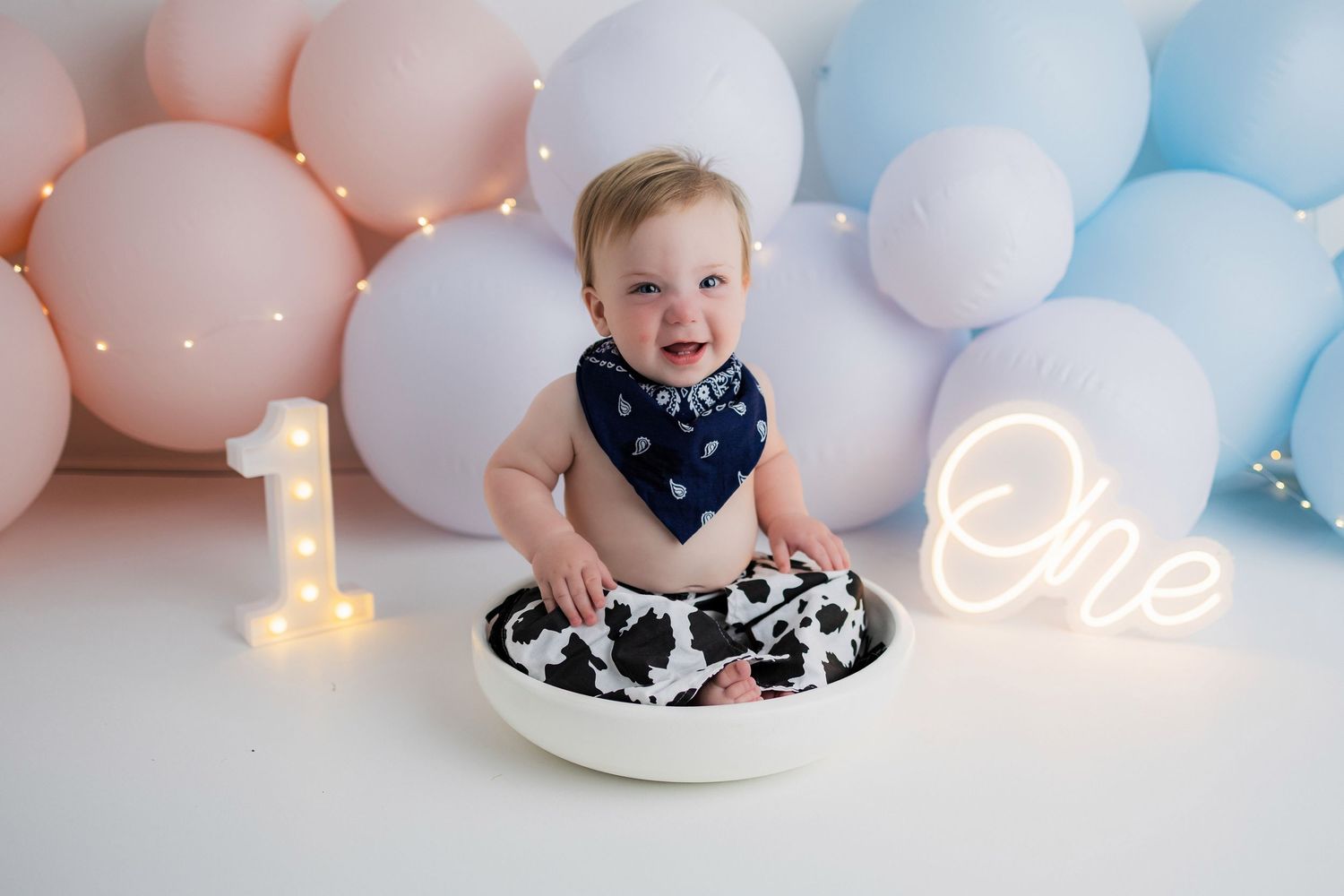 First birthday party decor with number one candle, pink and blue balloons, and cake smashing setup.
