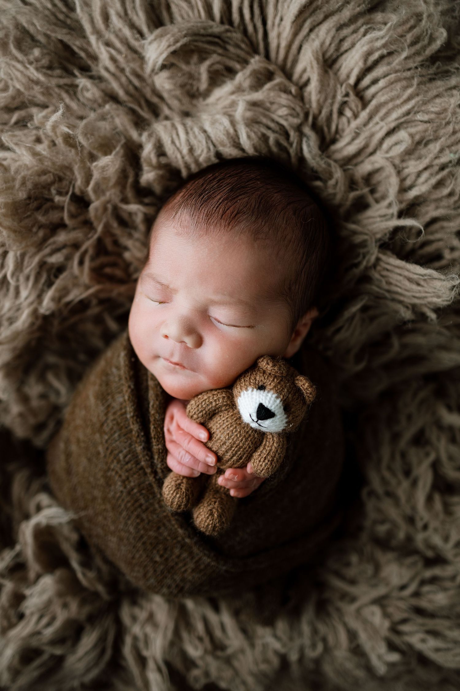 Sleeping newborn baby wrapped in brown knit blanket lying on fluffy beige fur rug in various peaceful poses.