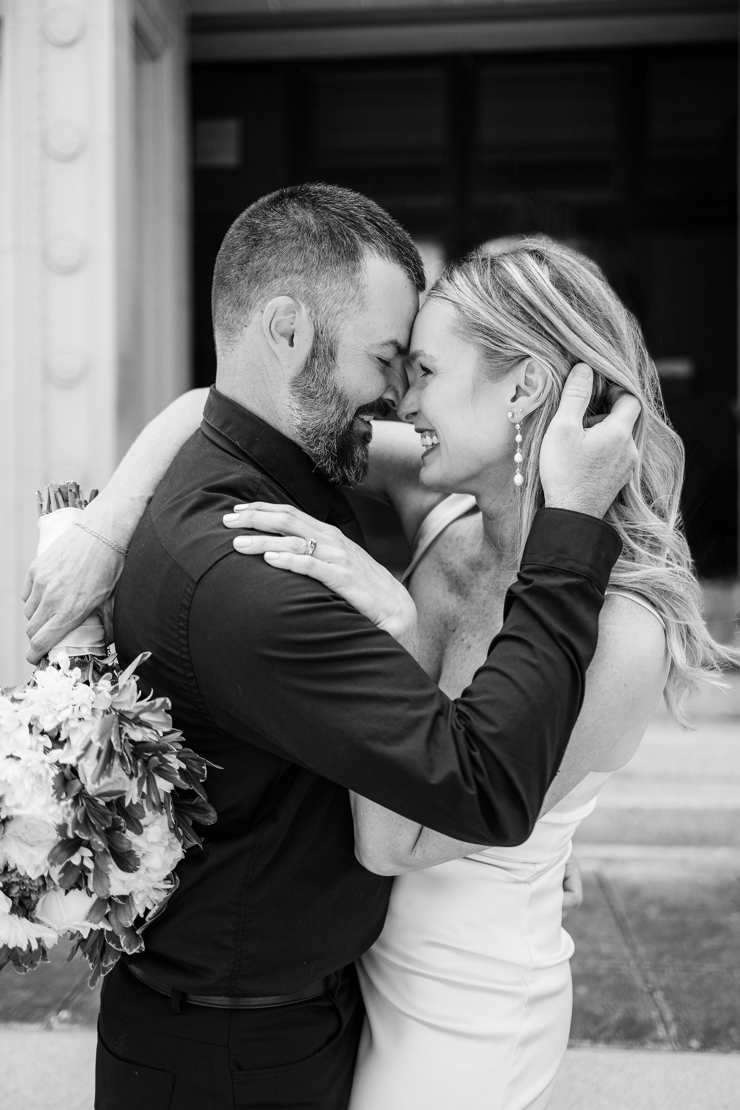 A romantic black and white wedding photo of a couple embracing, with the bride holding a floral bouquet.