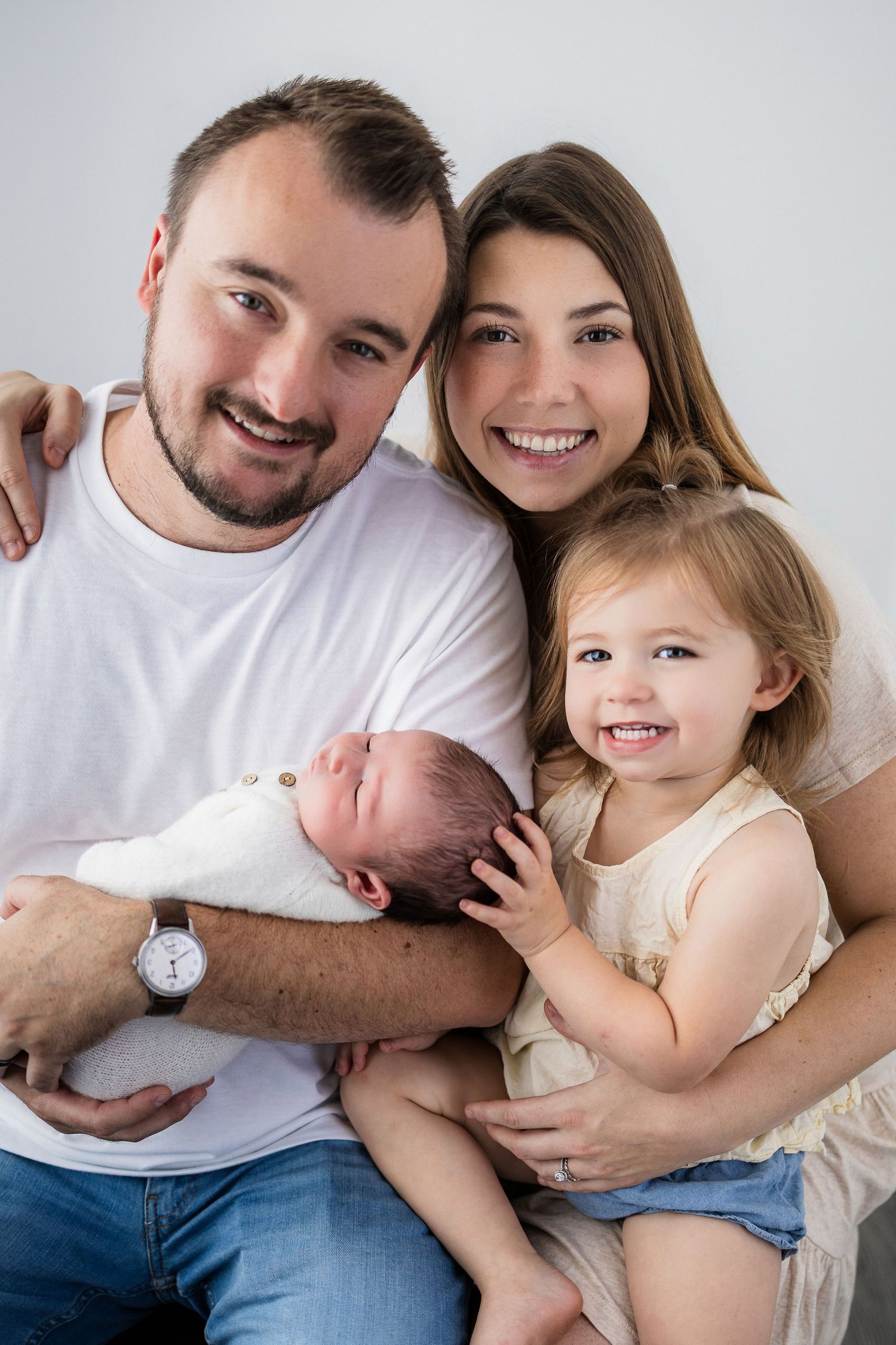 A happy family poses together with their newborn baby and young toddler for a heartwarming portrait.