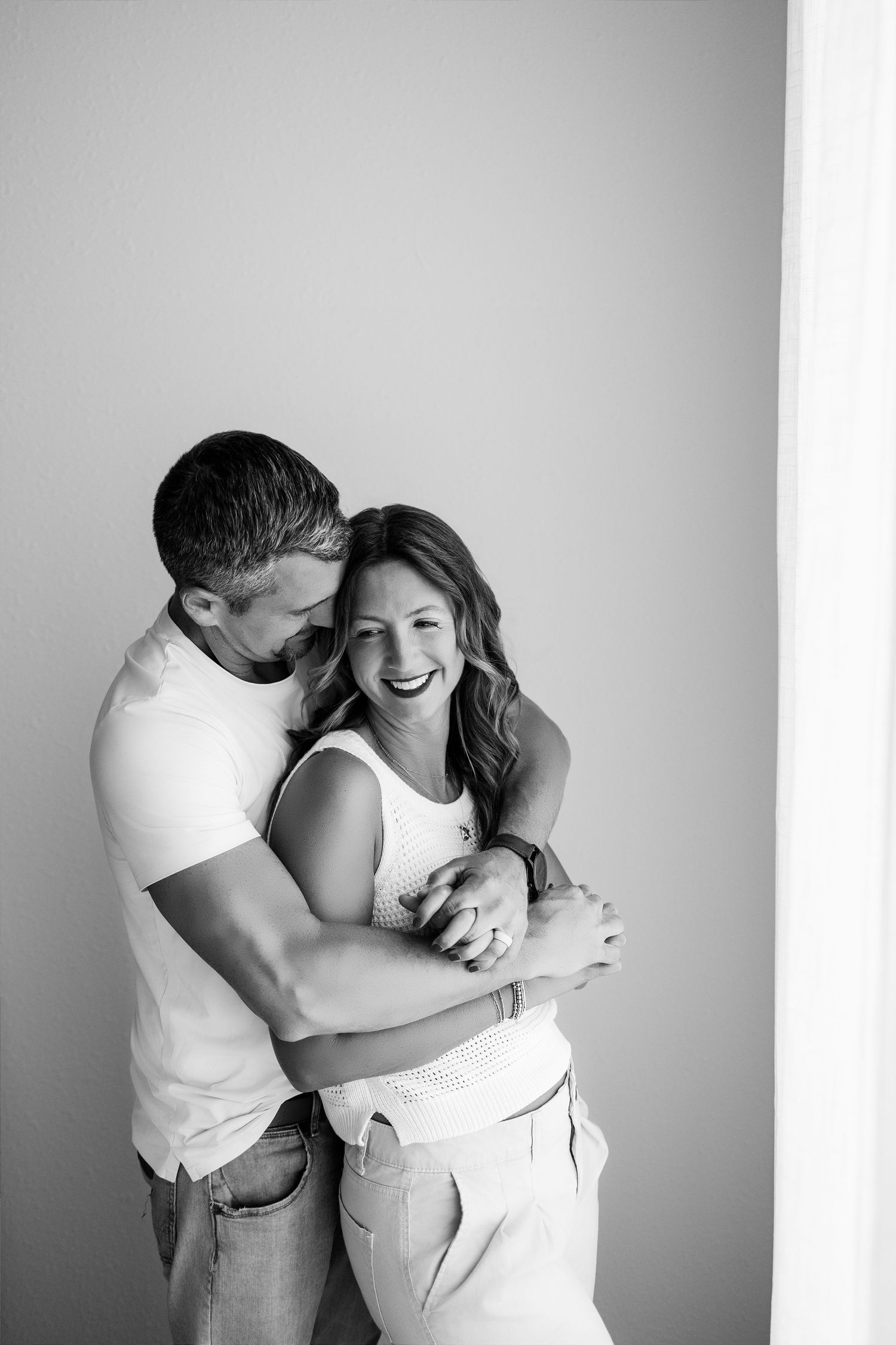 Black-and-white portrait of a podcasting couple laughing together during their studio branding session