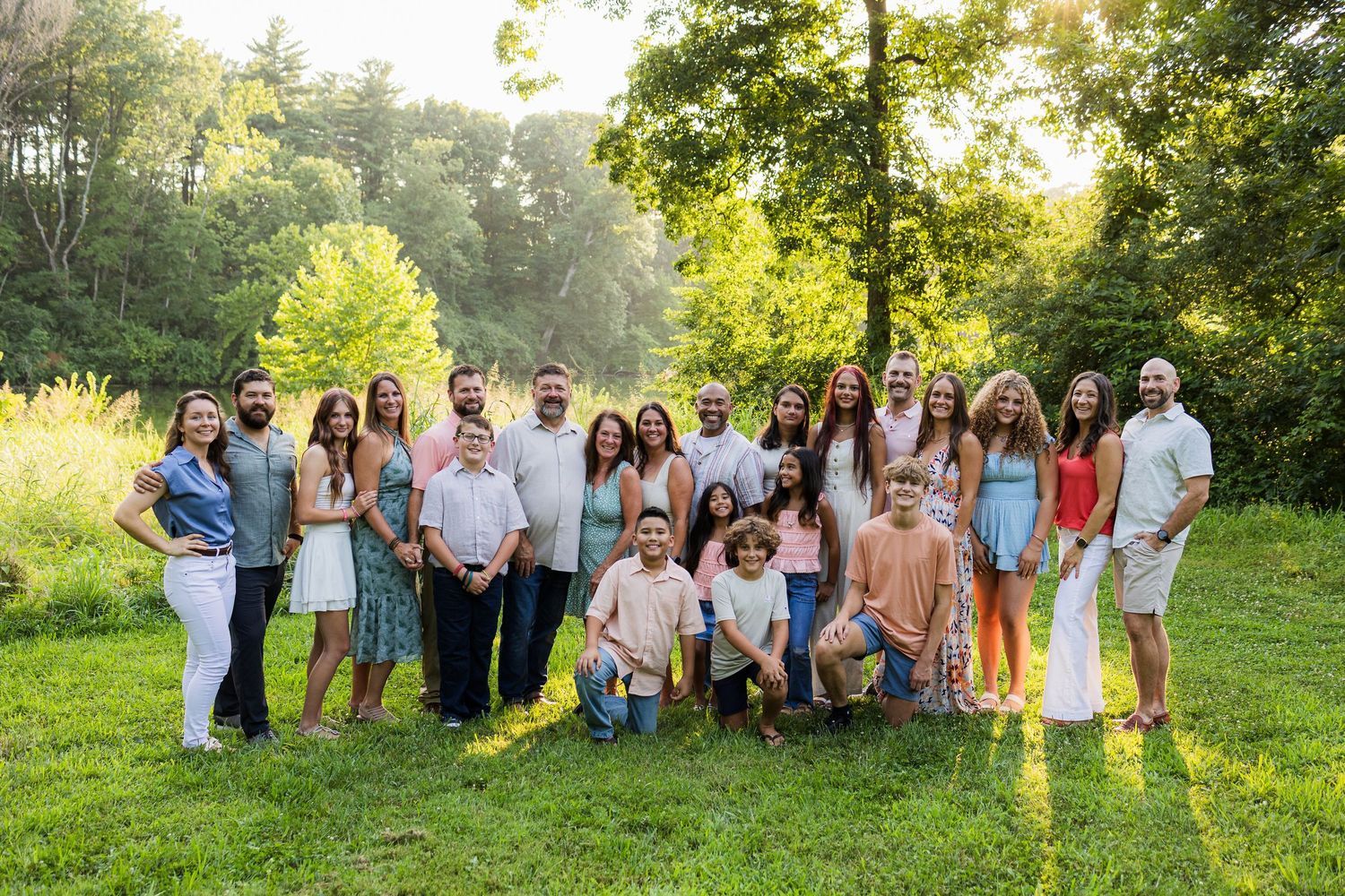 A group stands together on a grassy lawn with sunlit trees in the background during golden hour.