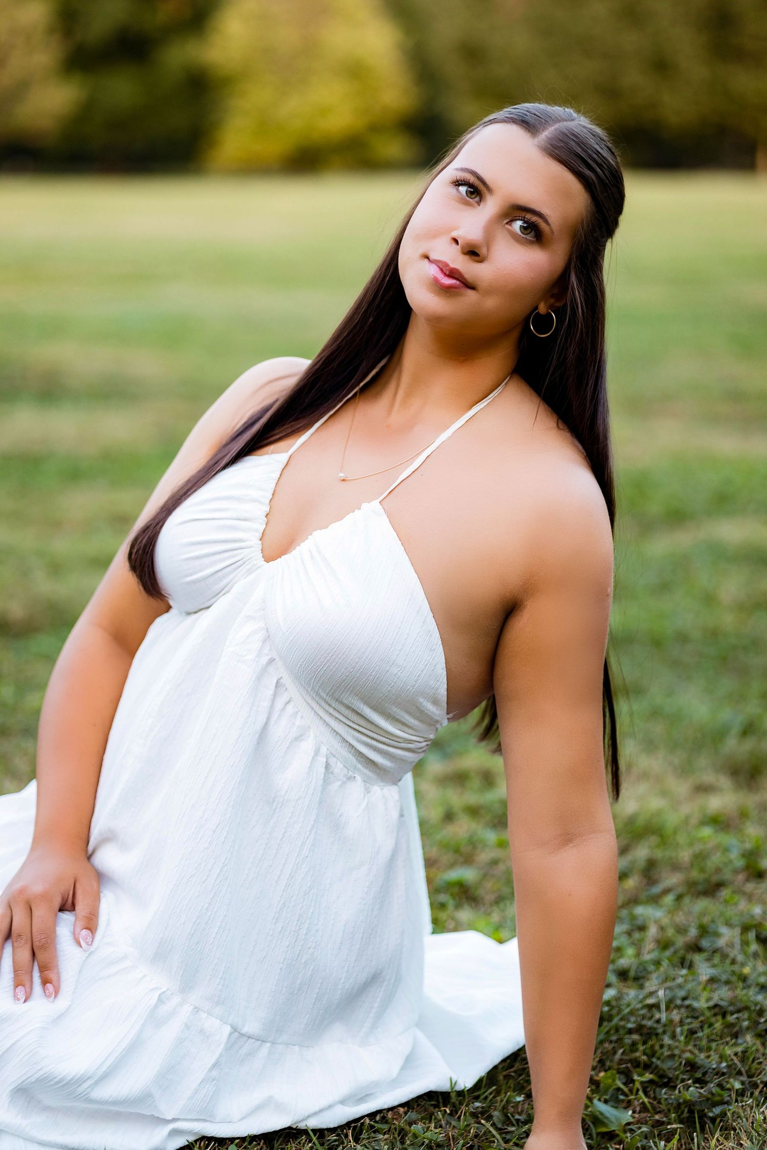 Woman in white sleeveless top poses gracefully on grass during outdoor portrait session.