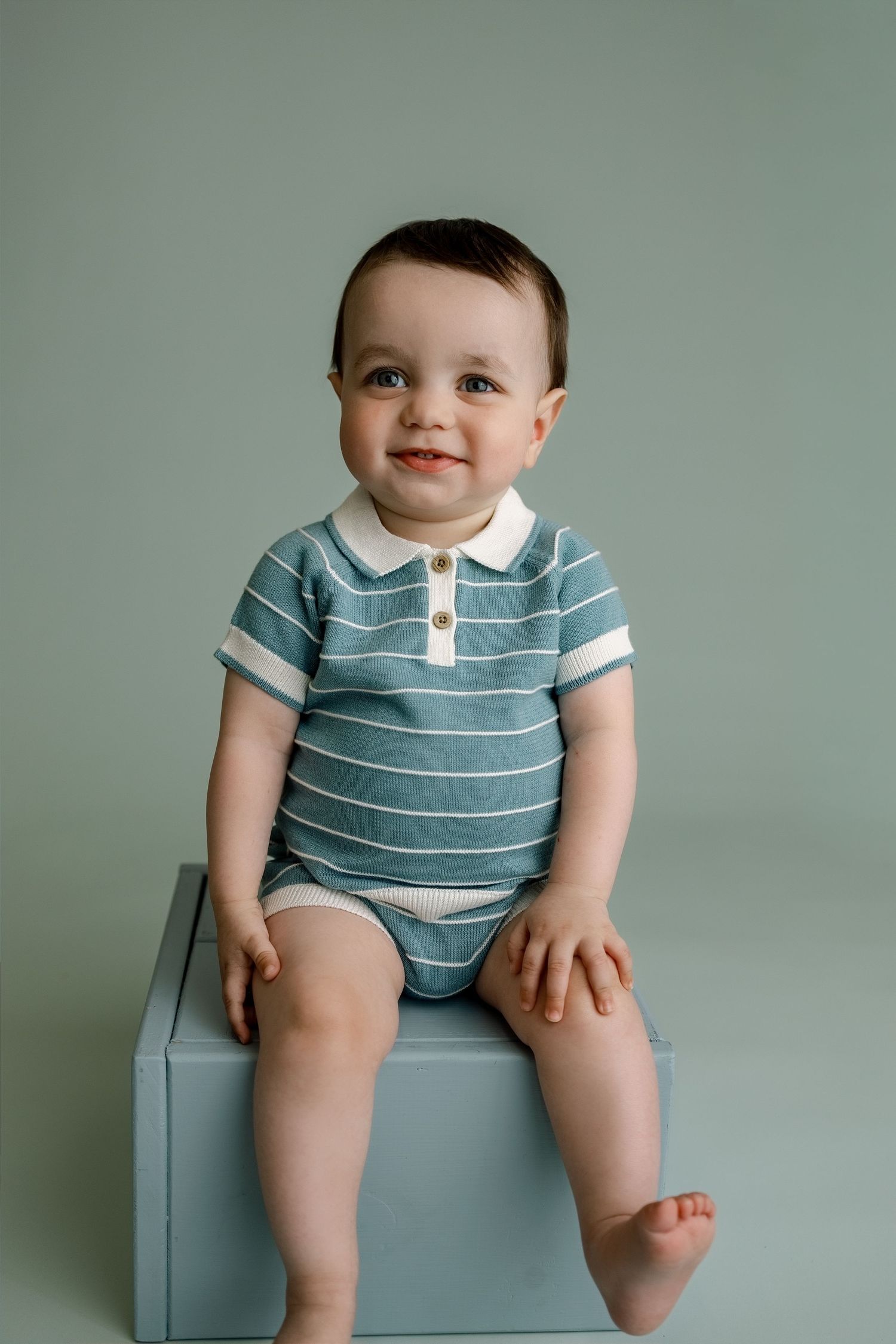 One-year-old boy smiling on a blue studio cube during an Edwardsville milestone photography session