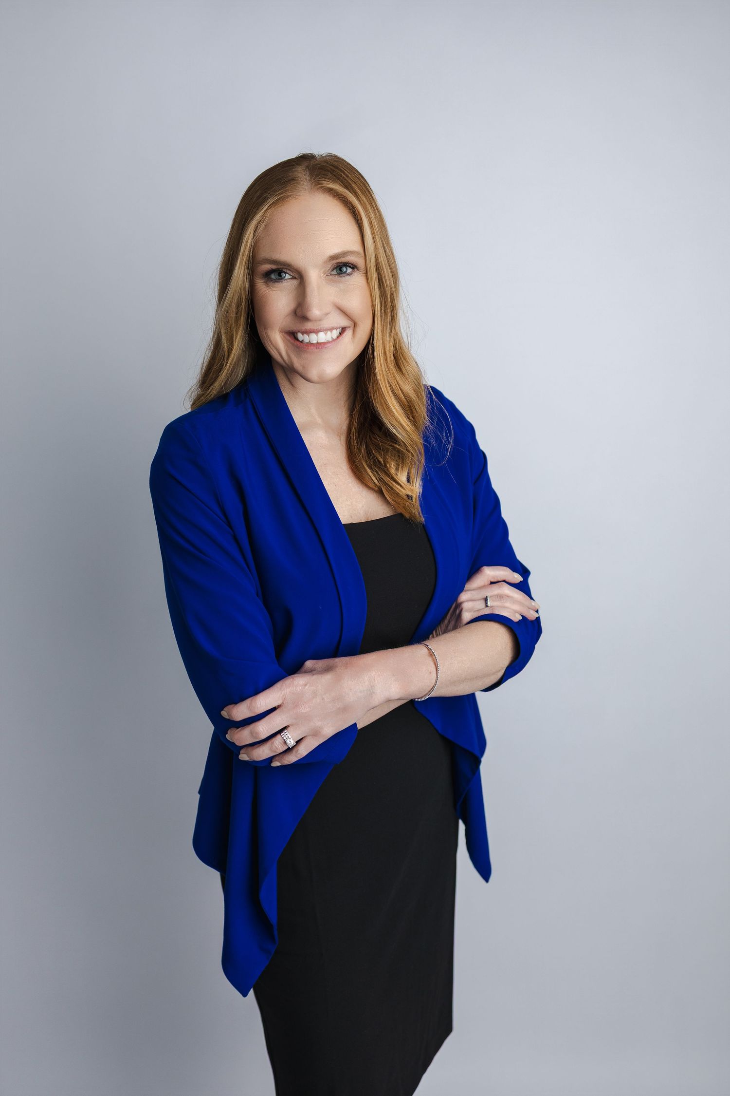 Professional portrait of person in royal blue blazer and black dress against grey background.