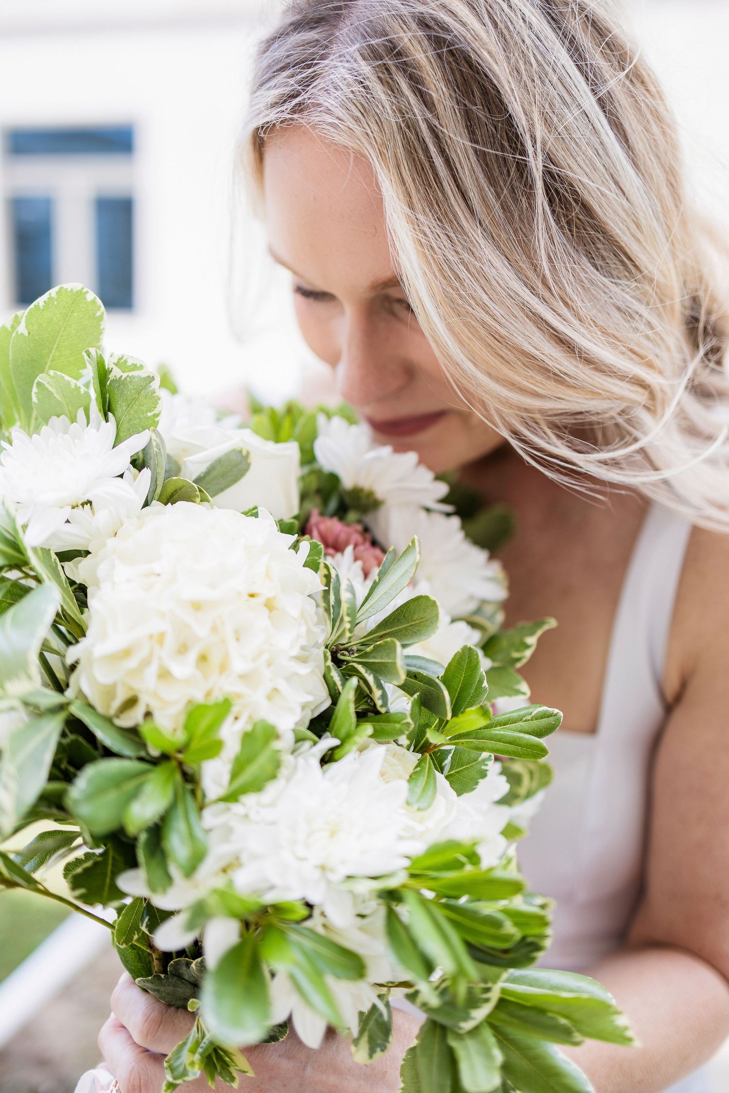 A blonde woman in white holds a beautiful bouquet of fresh white peonies and greenery.