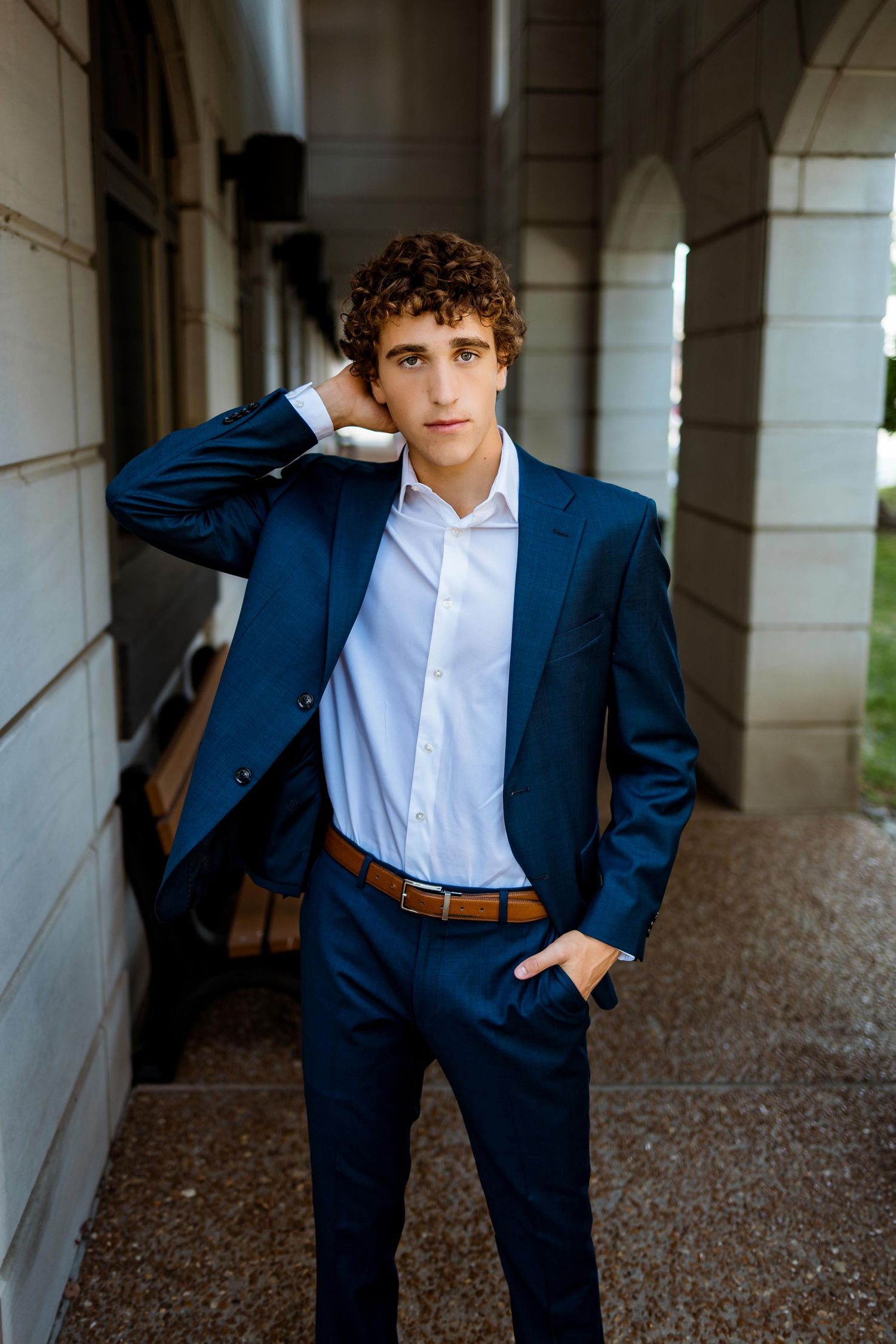 Multiple shots of someone in a navy suit and light blue shirt posing casually in an architectural setting.