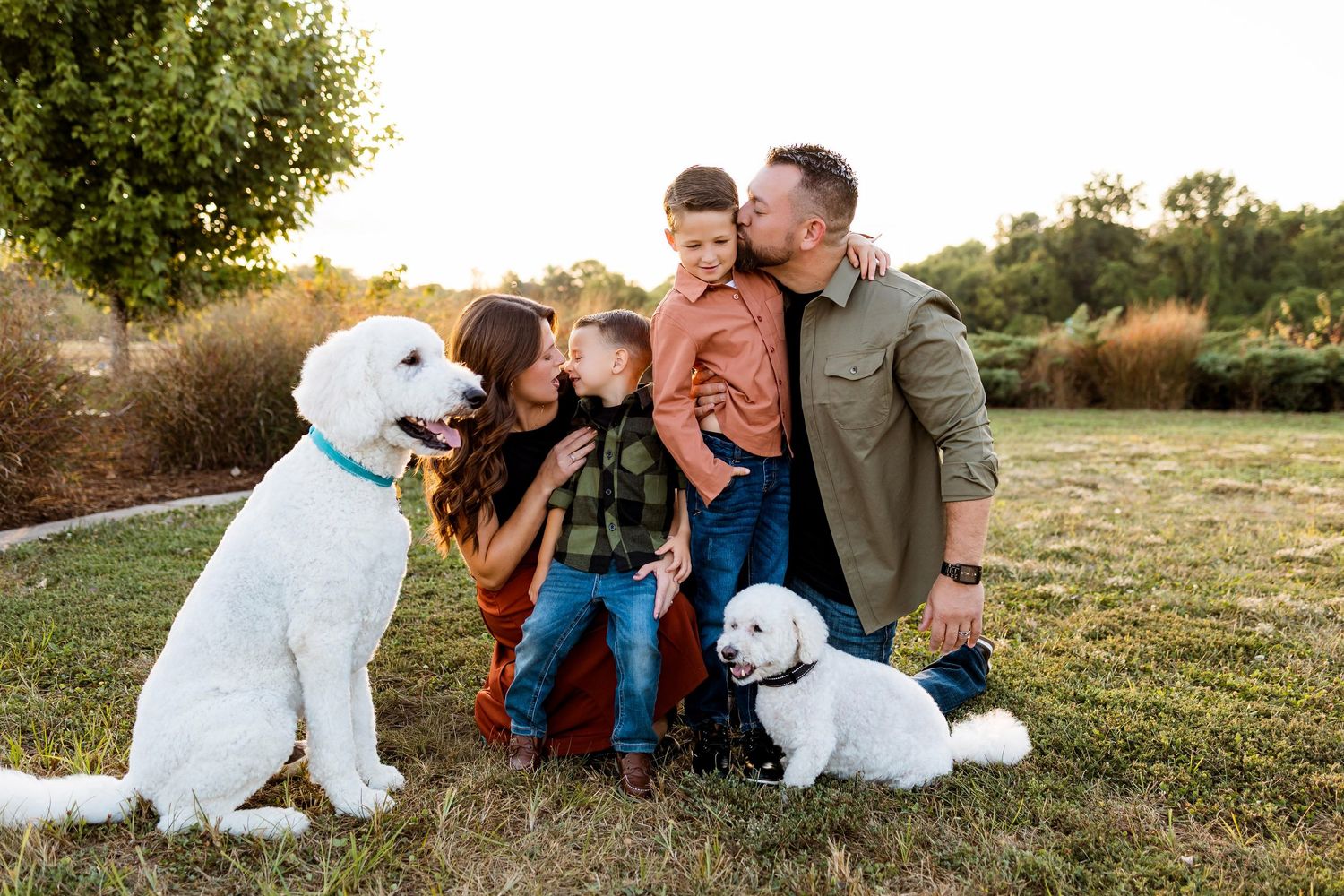 Family enjoying outdoor moments together with their white dog during golden hour in a grassy field.