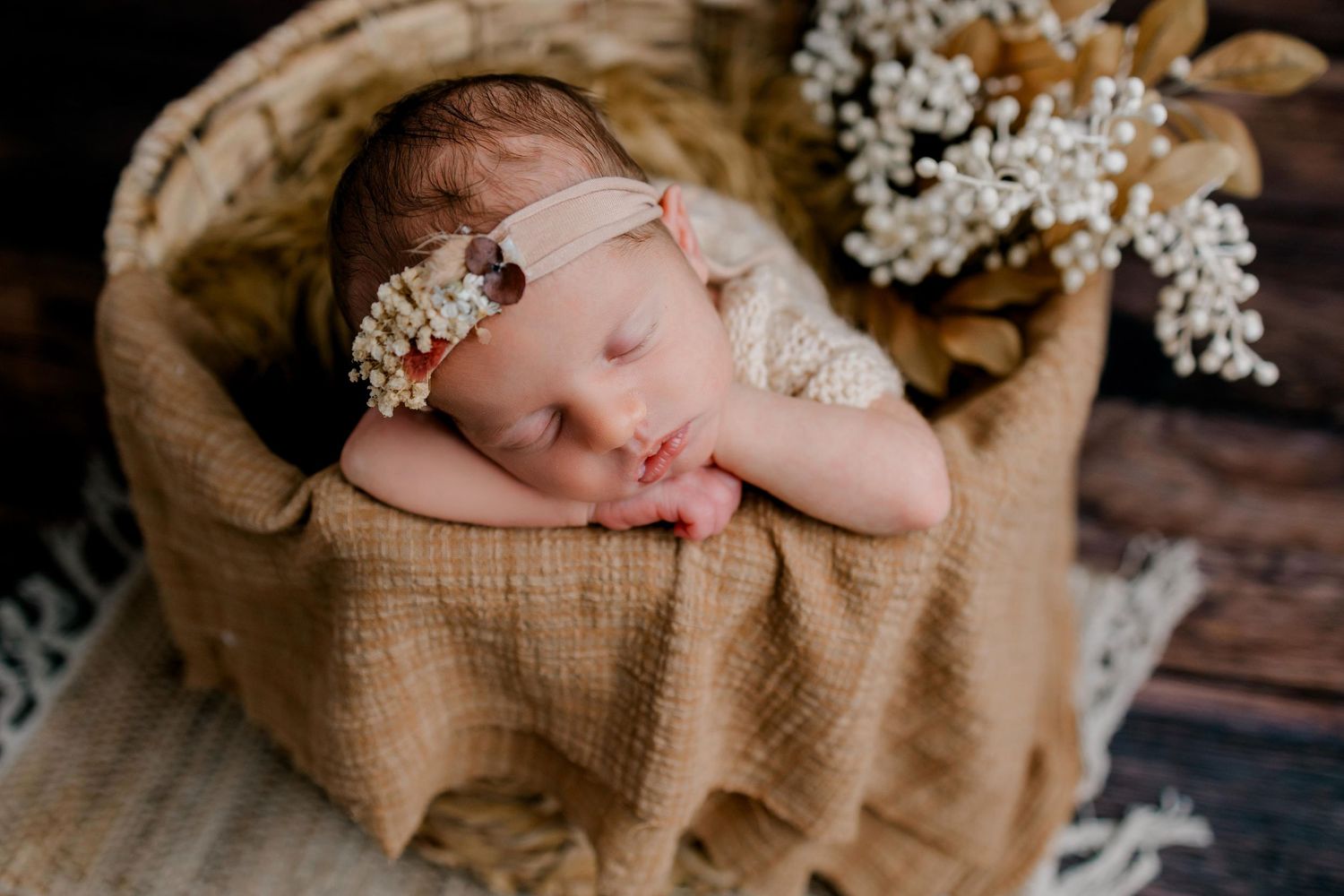 Sleeping newborn in rustic basket with delicate floral headpiece and burlap fabric.