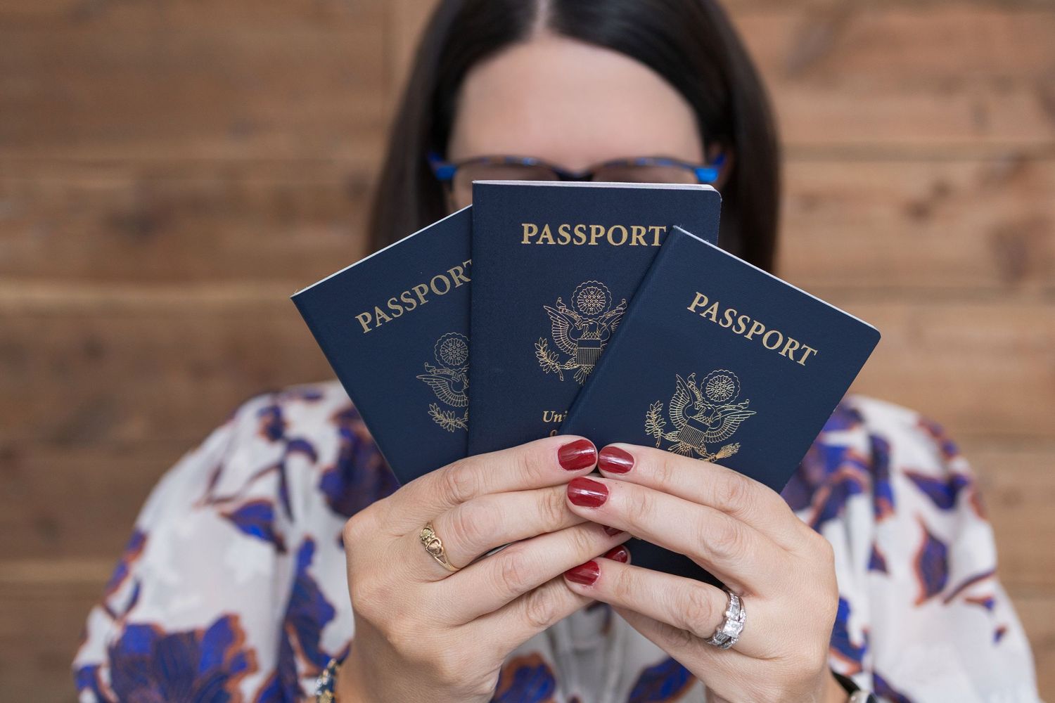 Hand with painted nails holds up a navy blue US passport against wooden background in sequence photos.