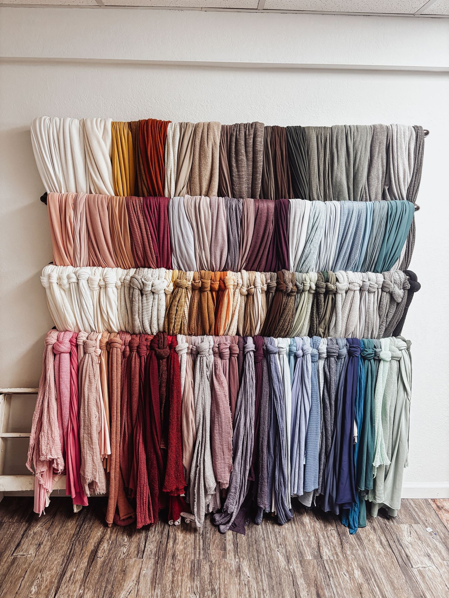 A collection of linen curtain panels arranged in a color gradient from light to dark hues displayed on a white wall.
