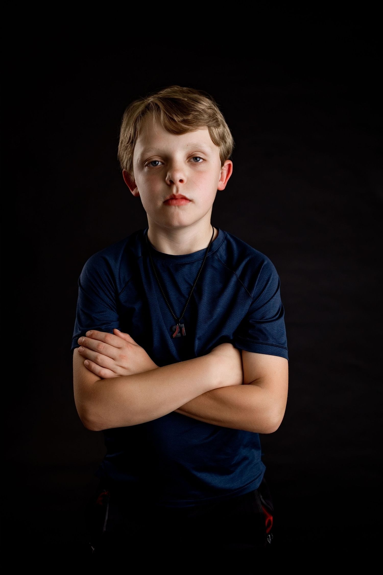 Young boy posing confidently with crossed arms against a dark studio backdrop in Edwardsville