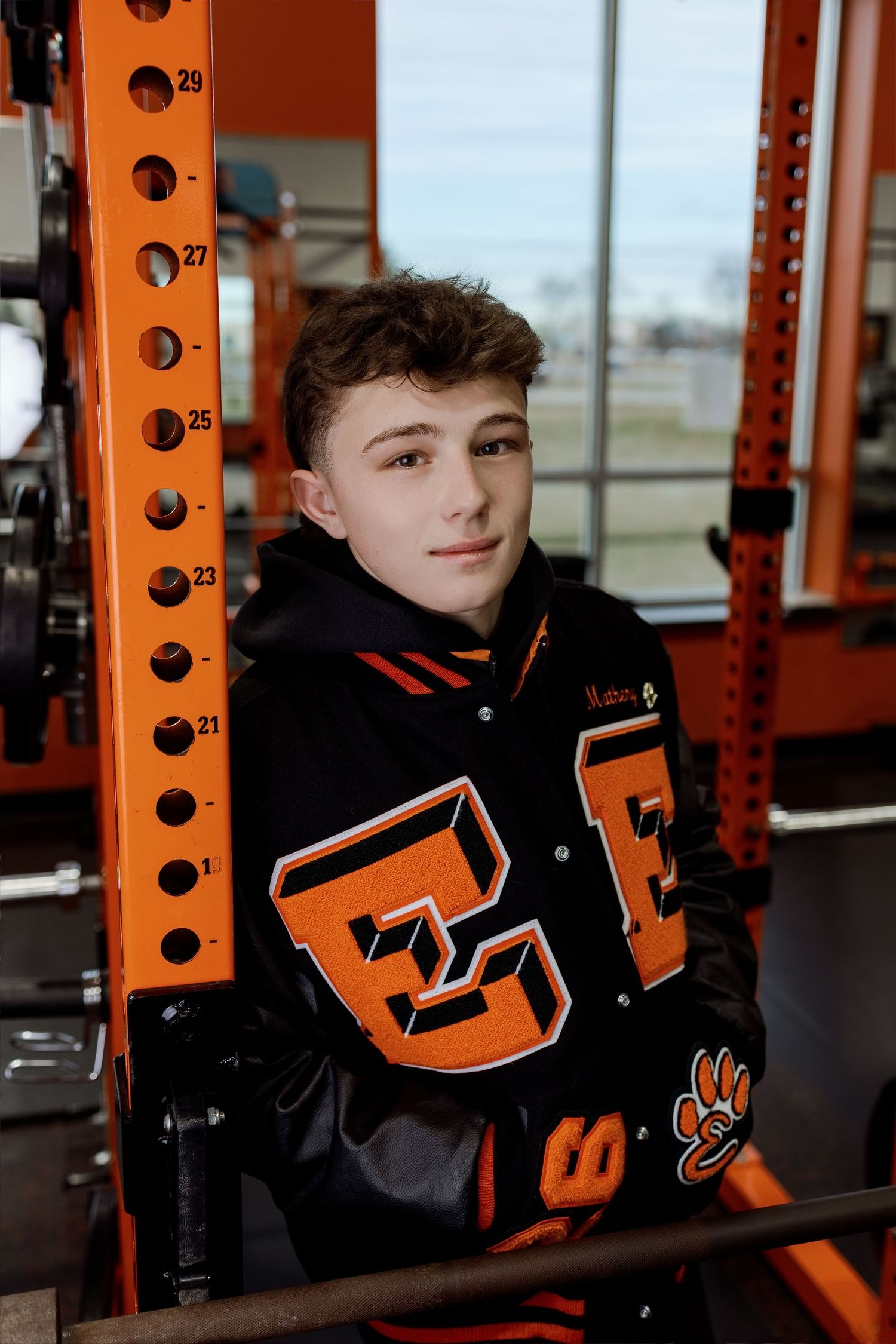 Student athlete poses in orange and black weight training facility wearing dark athletic gear.