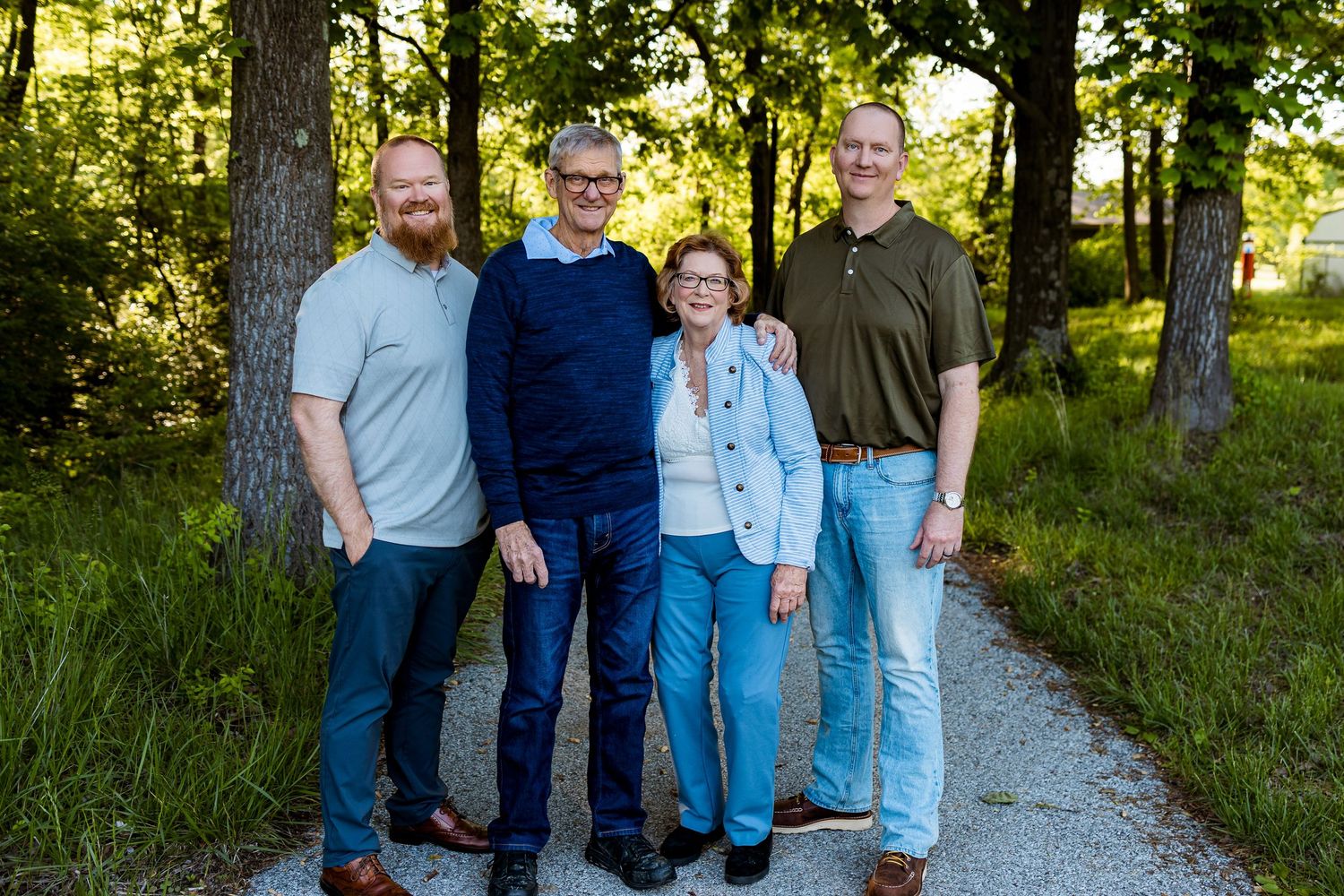 Four adults standing together on a gravel path with trees in natural lighting.