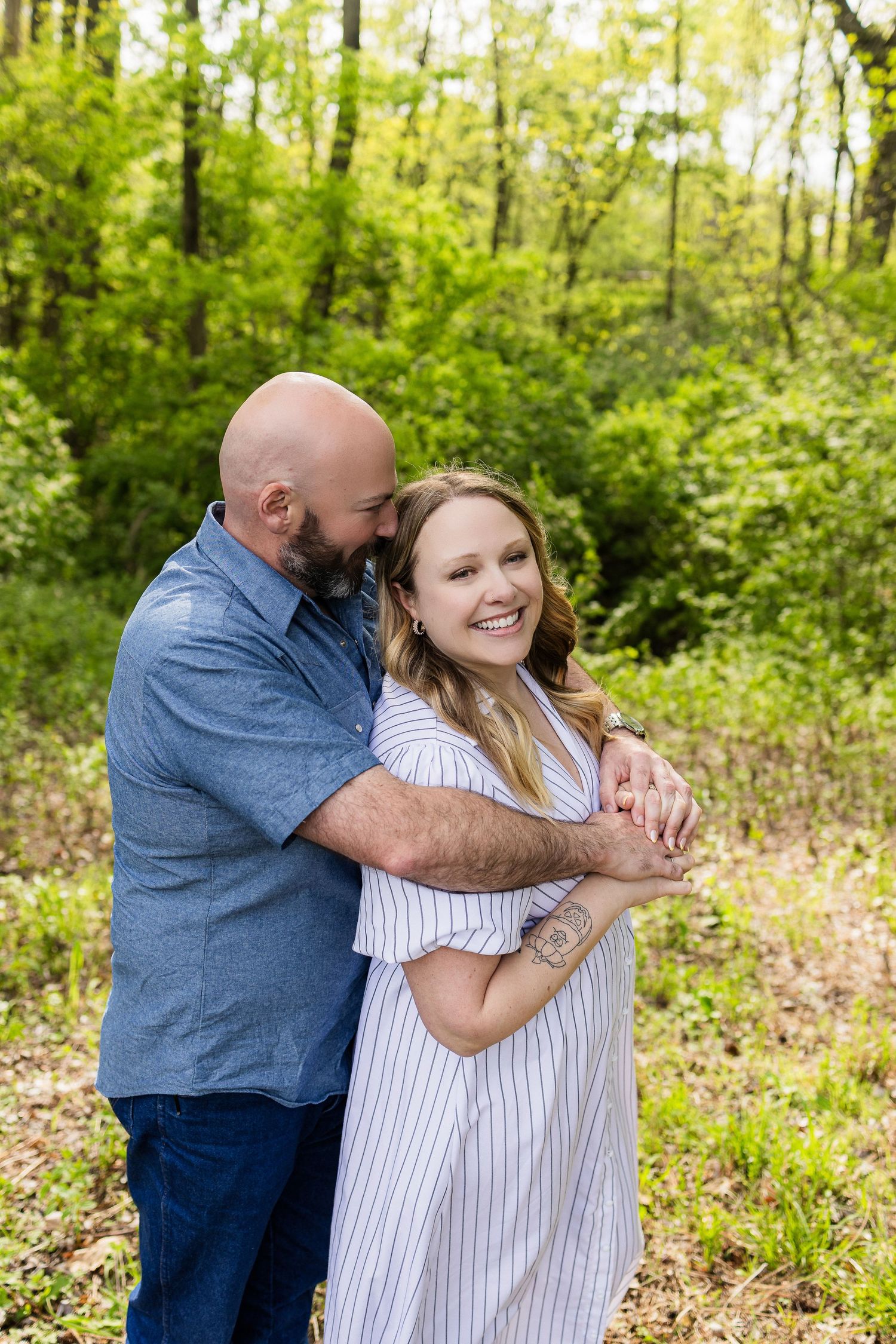 Couple sharing an intimate embrace in a sunlit wooded area.
