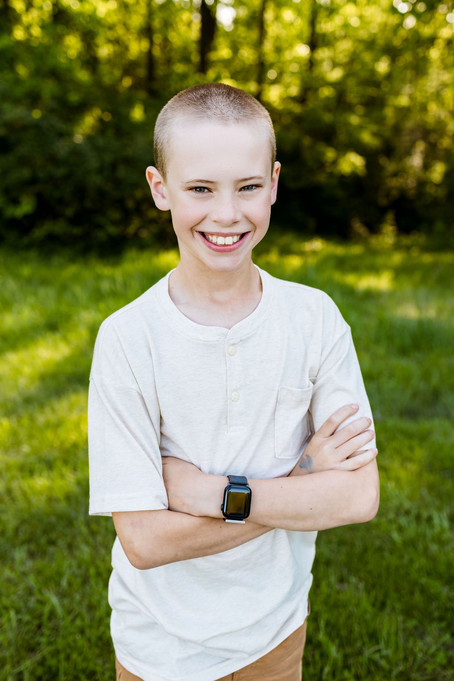 Cheerful youth wearing white t-shirt and smart watch poses with crossed arms in sunny outdoor setting.