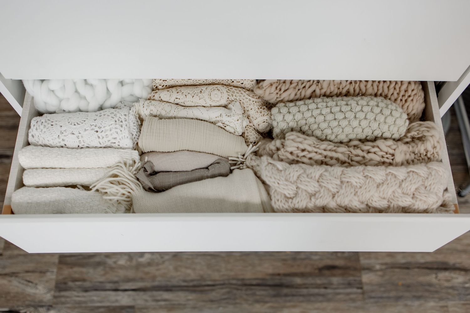 Neatly folded cozy knit blankets and throws in neutral beige and cream colors organized in a white drawer.