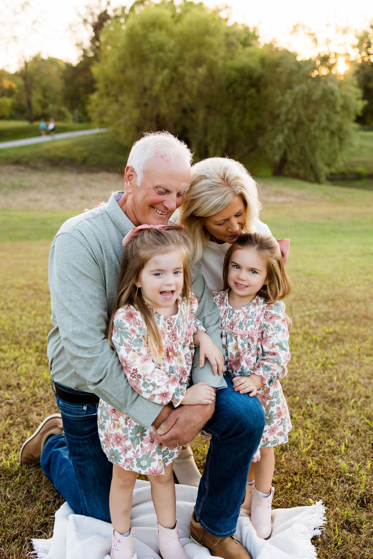 Family embraces and laughs together on grassy field during outdoor photo session.