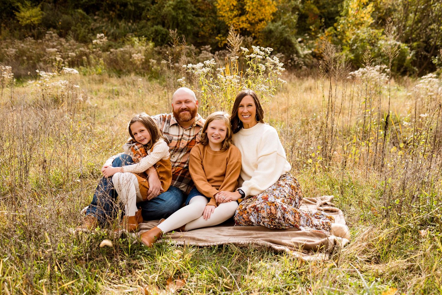 People lounging on blankets in a rustic fall field surrounded by warm autumn colors.