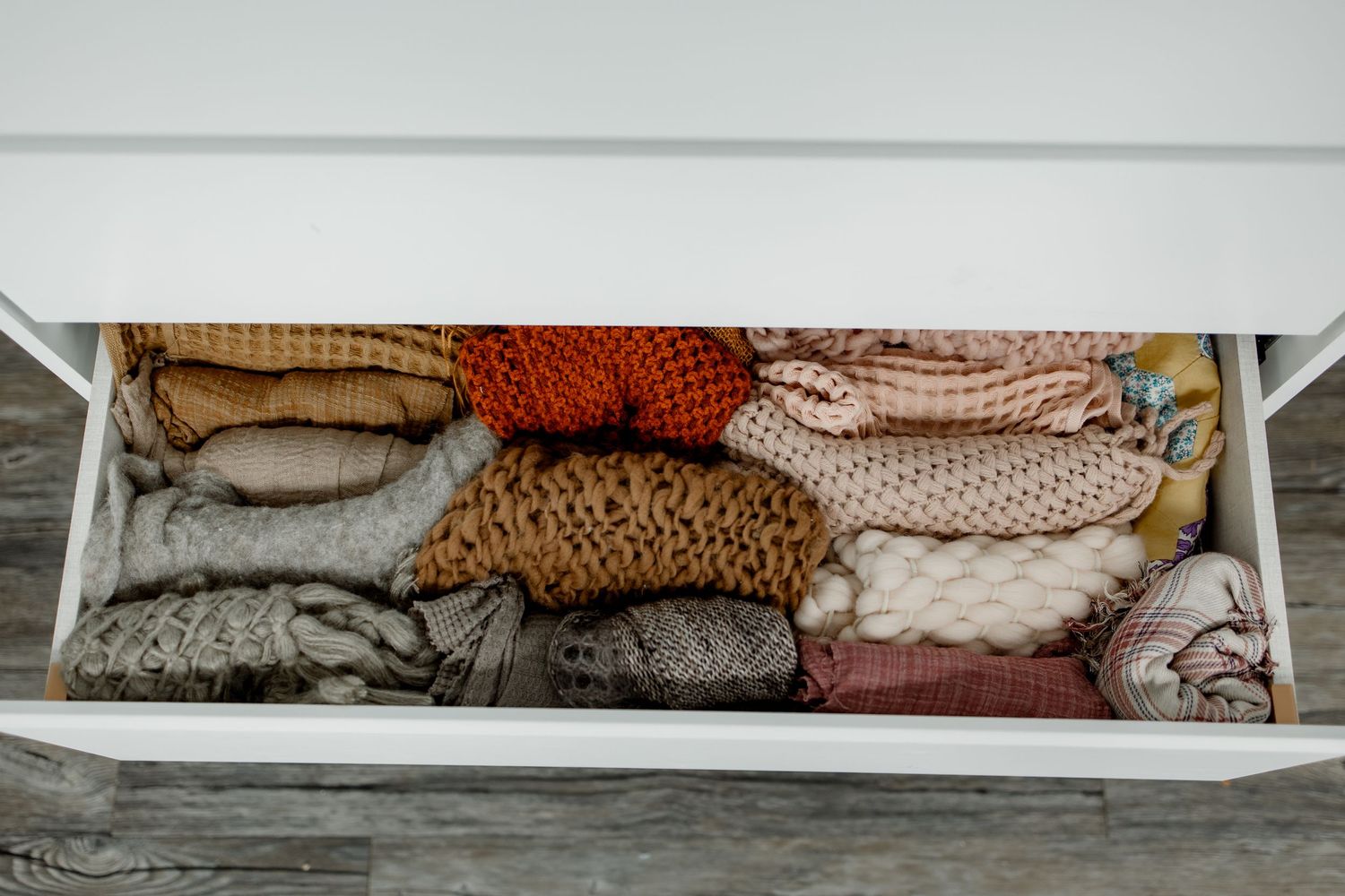 Neatly folded textiles and linens stacked on white shelves displaying various neutral and earthy colored fabrics.