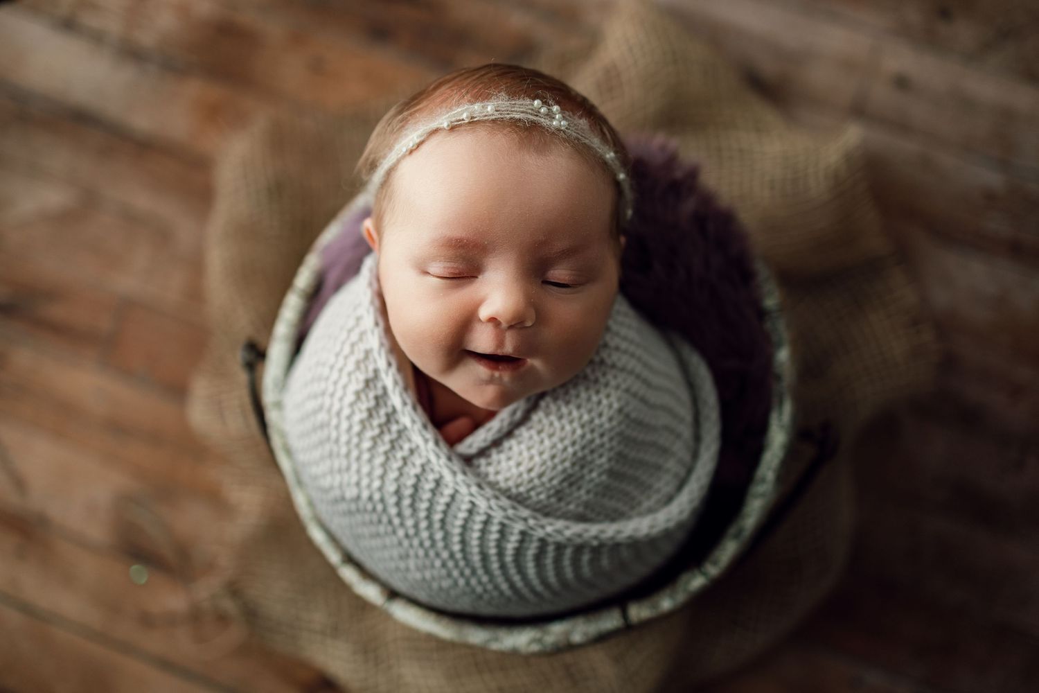 A sleeping baby swaddled in soft gray knit fabric against a rustic wooden background.