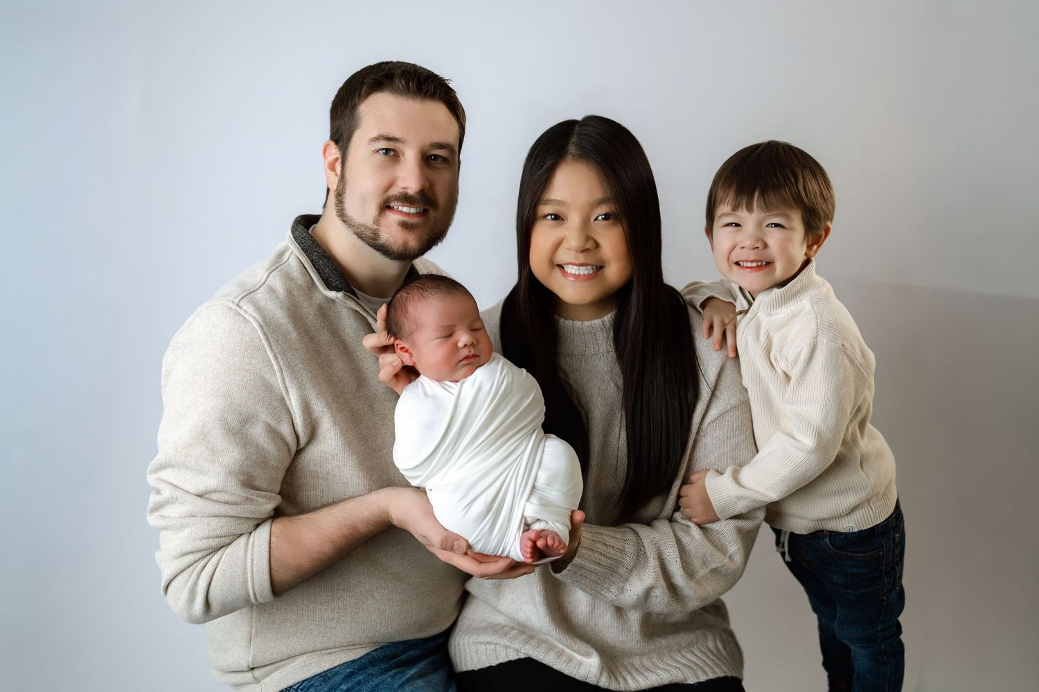 A family wearing coordinated cream colored outfits poses together on a light neutral background.