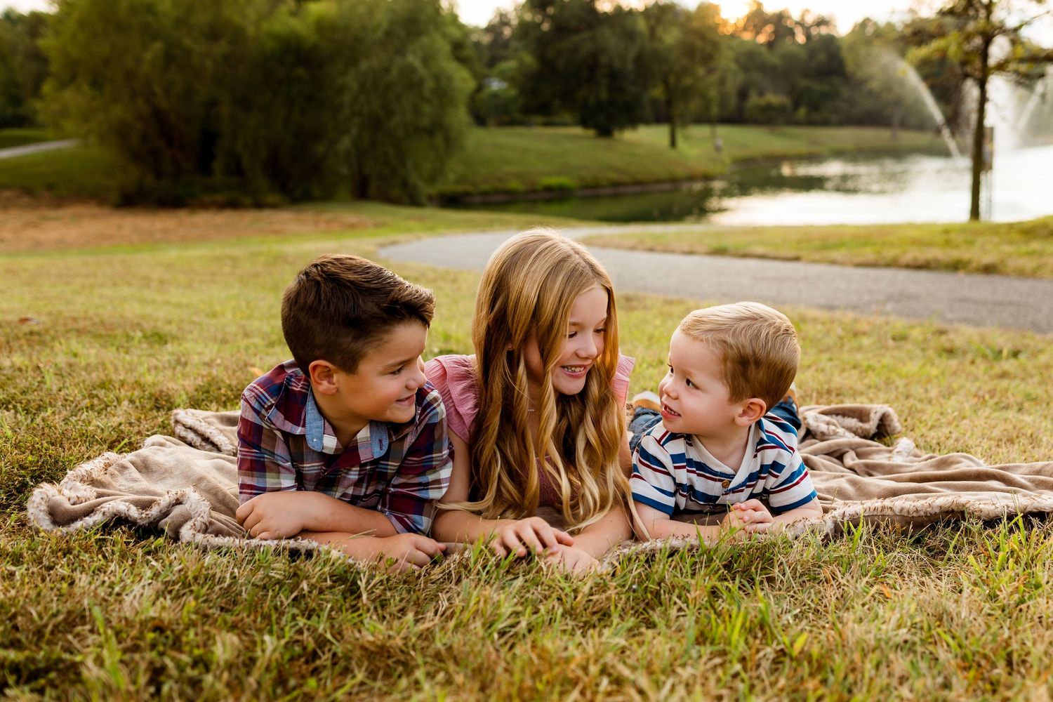 Family members lying on grass in a park during golden hour enjoying quality time together outdoors.