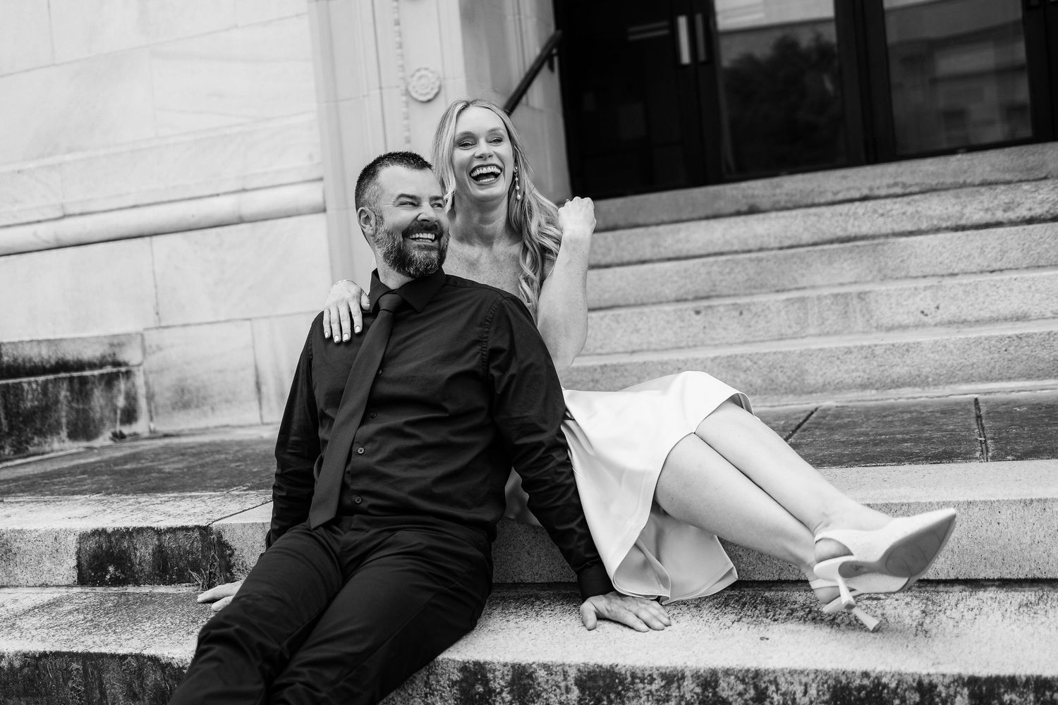 Black and white photo of a couple sharing a joyful moment while sitting on stone steps.