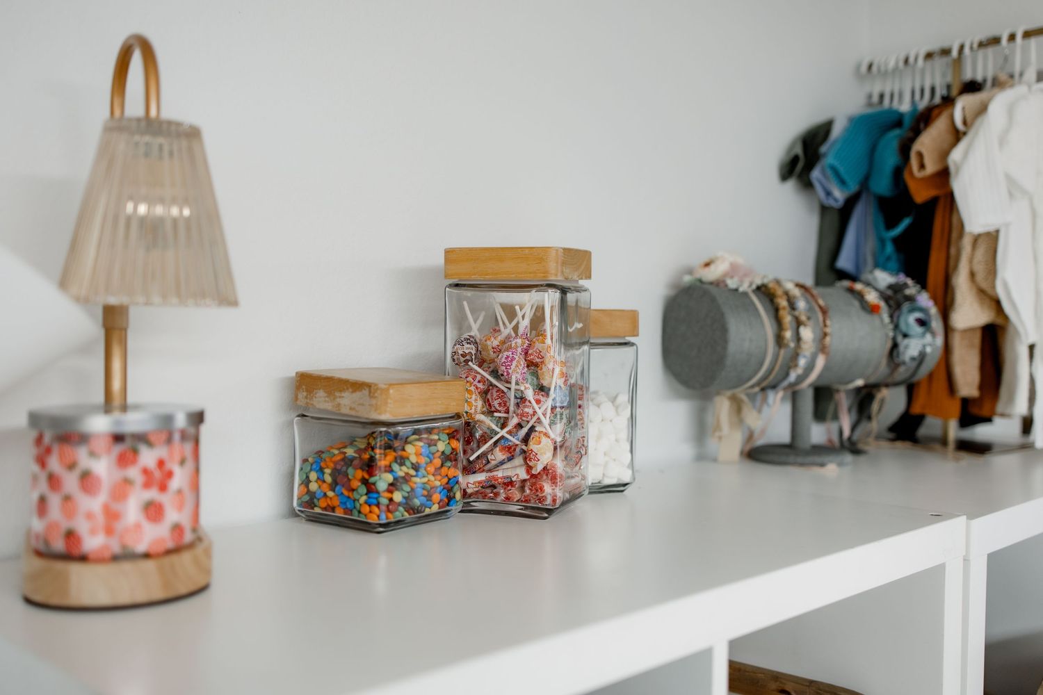 Decorative glass storage jars and a table lamp arranged on a white shelf with vintage-style home accessories.