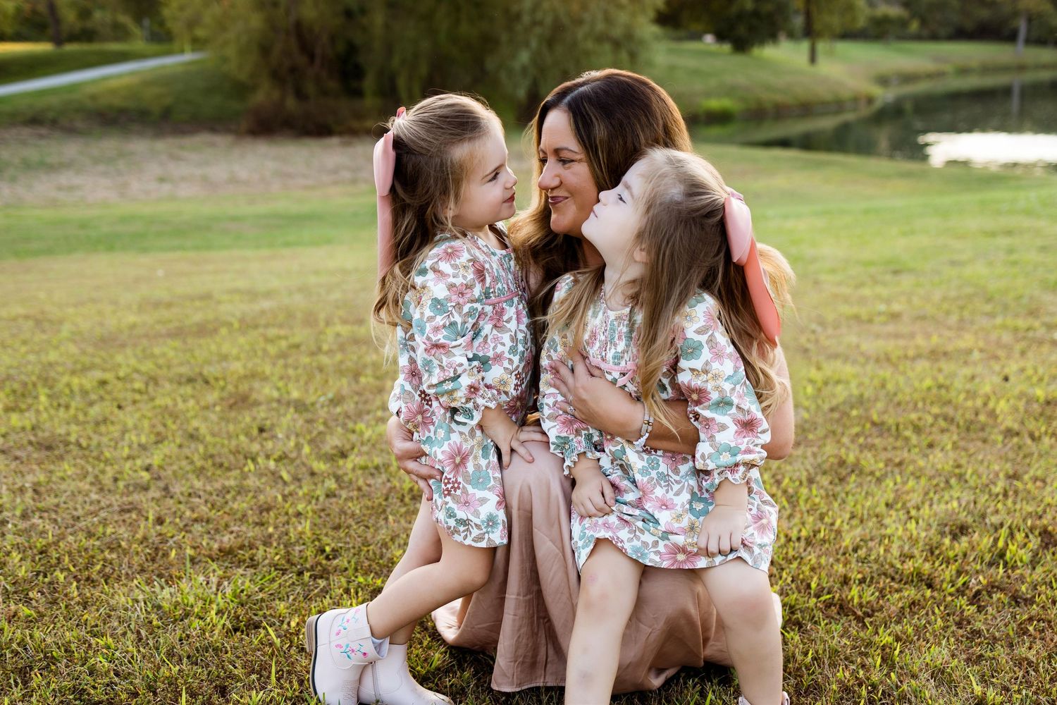 A tender outdoor family moment with matching floral dresses on a sunny grassy field.